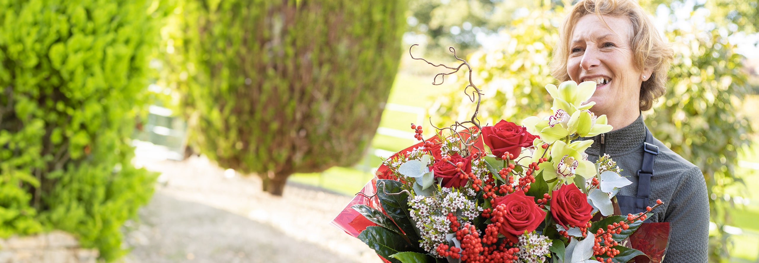 Florist holding a festive bouquet of red roses and seasonal flowers outdoors.