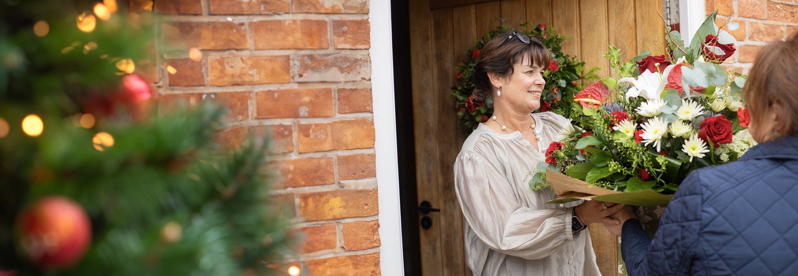 Woman receiving a festive bouquet of flowers at their doorstep.