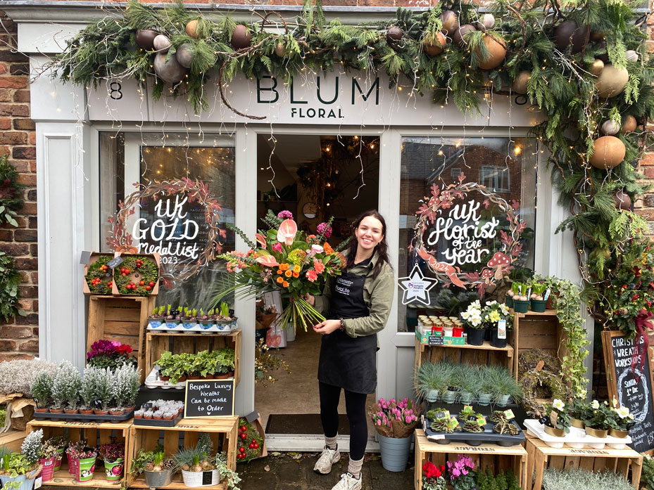 Blum Floral's Kirsty Noble smiling and holding a bouquet in front of her flower shop