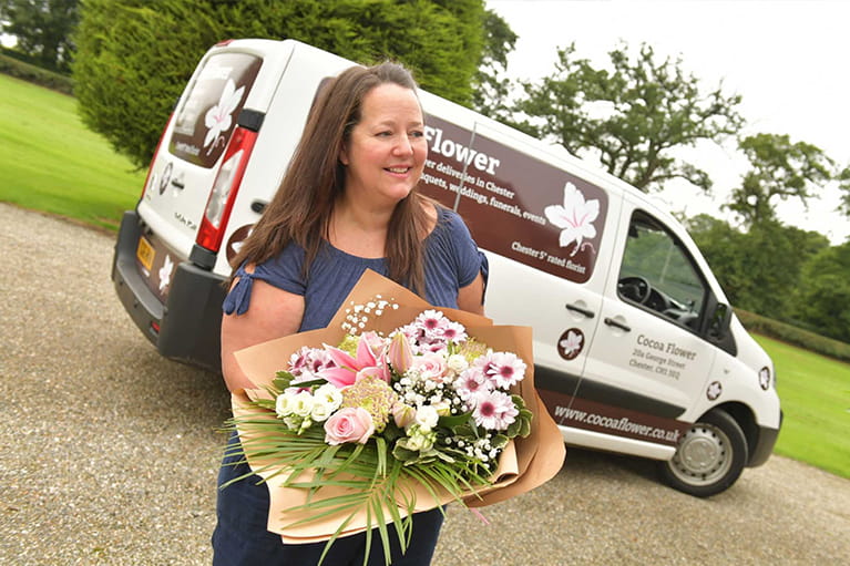 Local florist holding bouquet beside delivery van