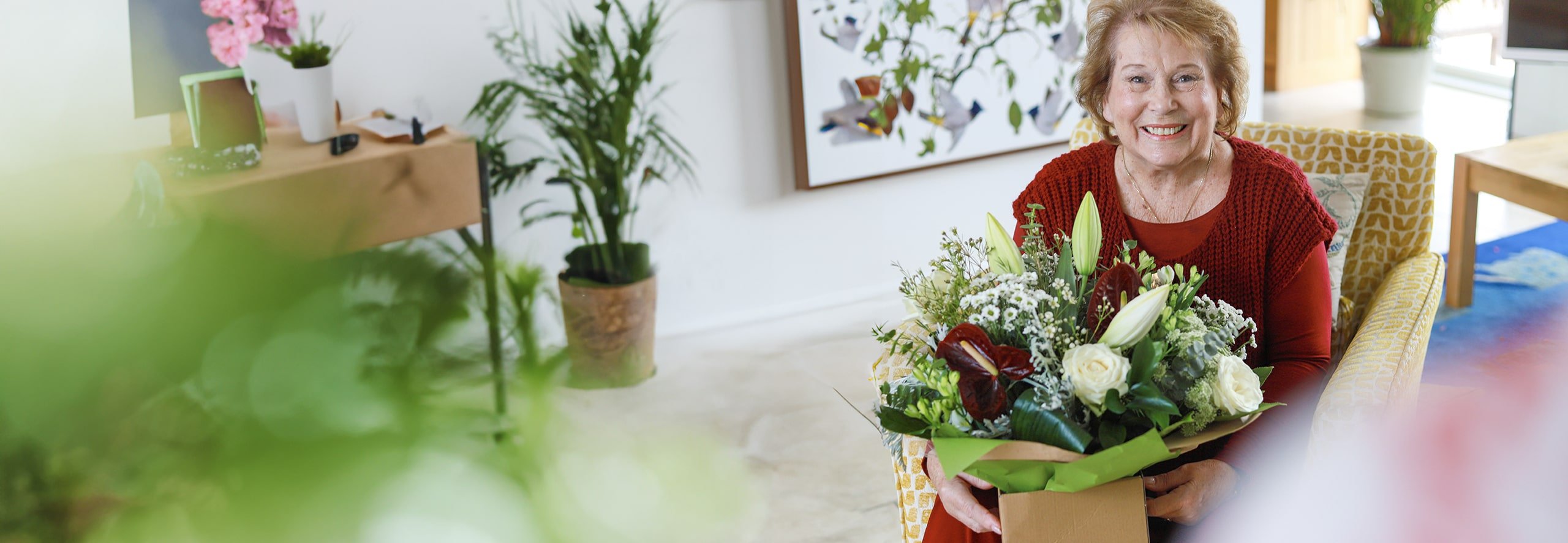 Person sitting indoors smiling while holding a fresh bouquet of flowers in a gift box