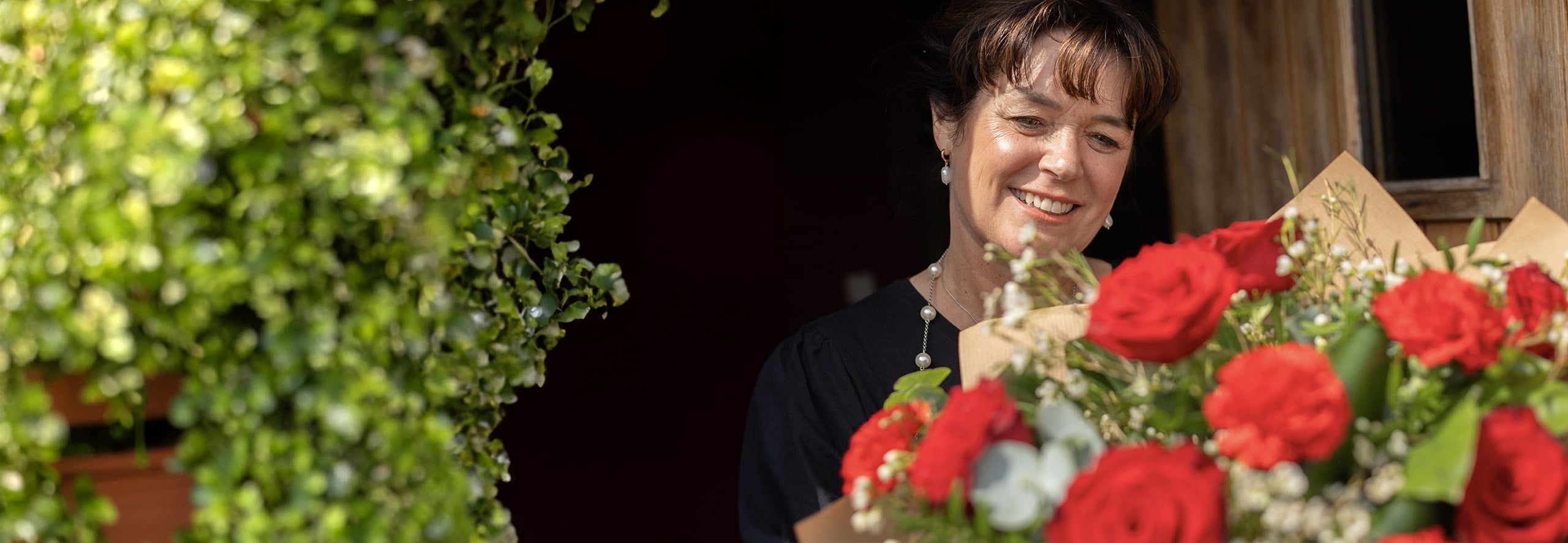 Woman smiling as she receives a bouquet of red roses at her front door.
