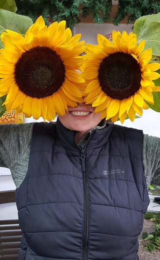 Florist playfully holding two large sunflowers in front of their face