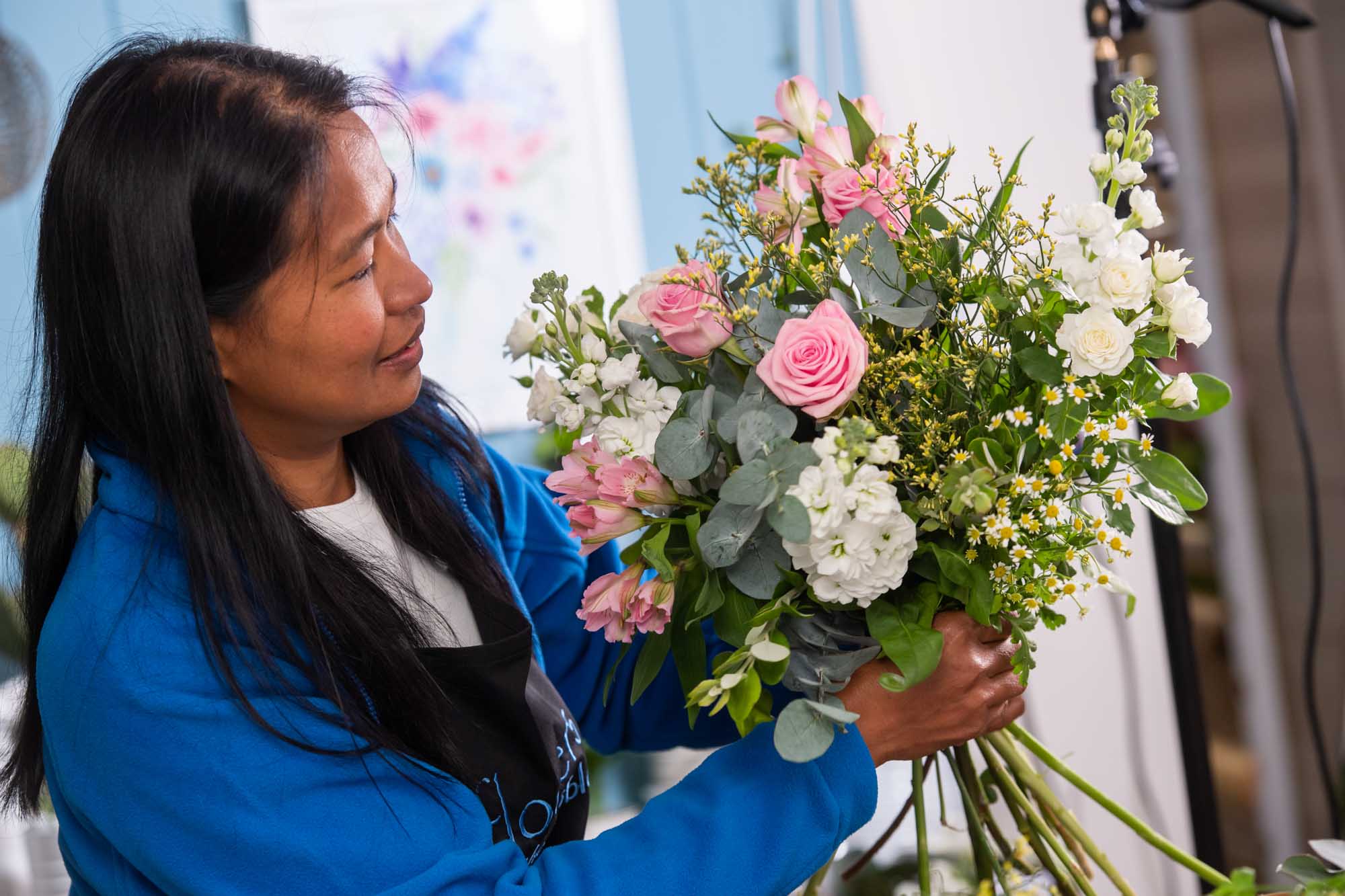 Florist wearing blue jacket making a pink a white handtied in a flowershop