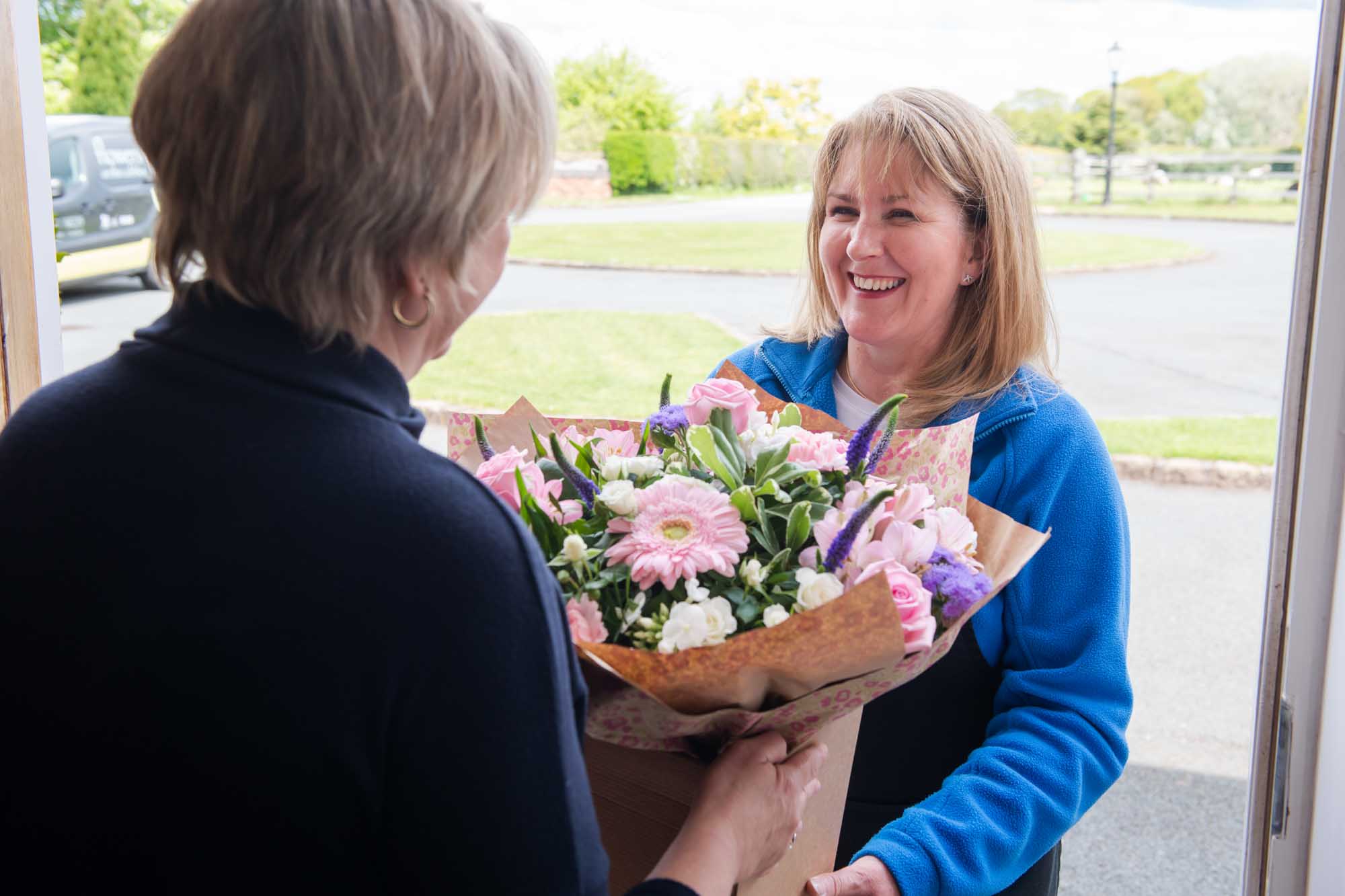 Woman recipient facing a happy woman florist holding a pink and purple bouquet she's delivering.