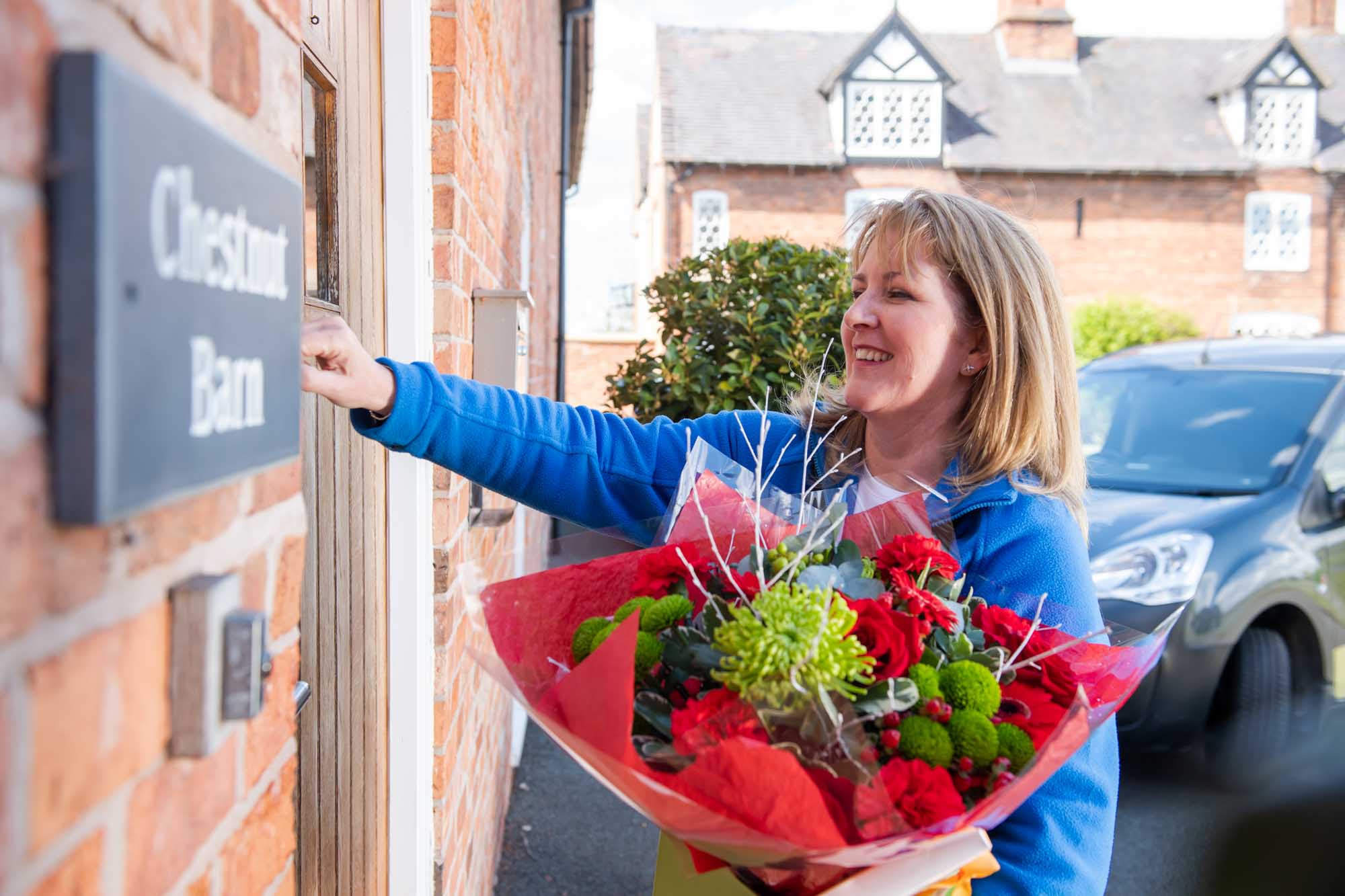 Smiling florist at front door holding a red themed Christmas Bouquet ringing the door bell