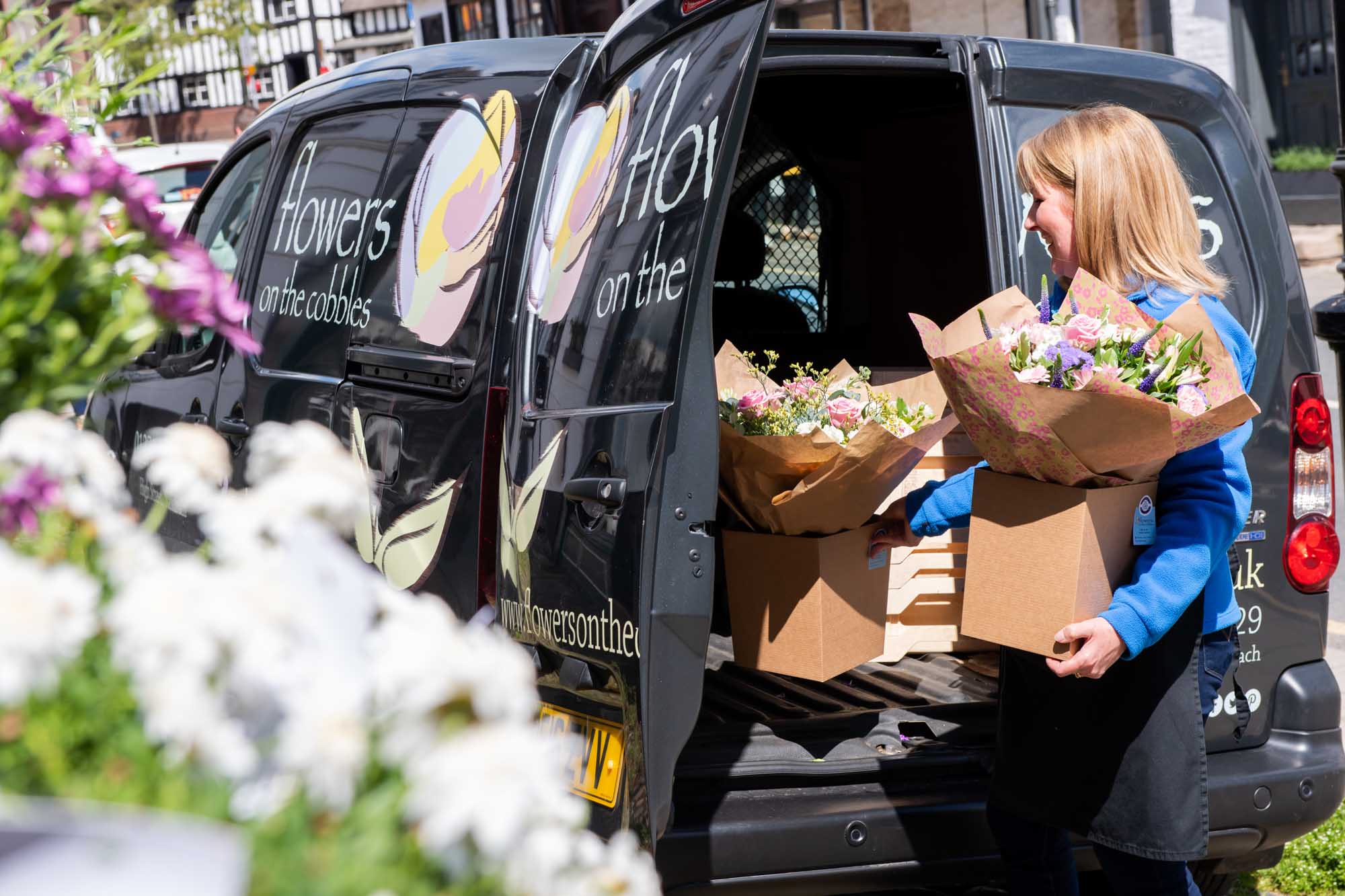 Florist putting two similar boxed hand-tieds into the back of her van