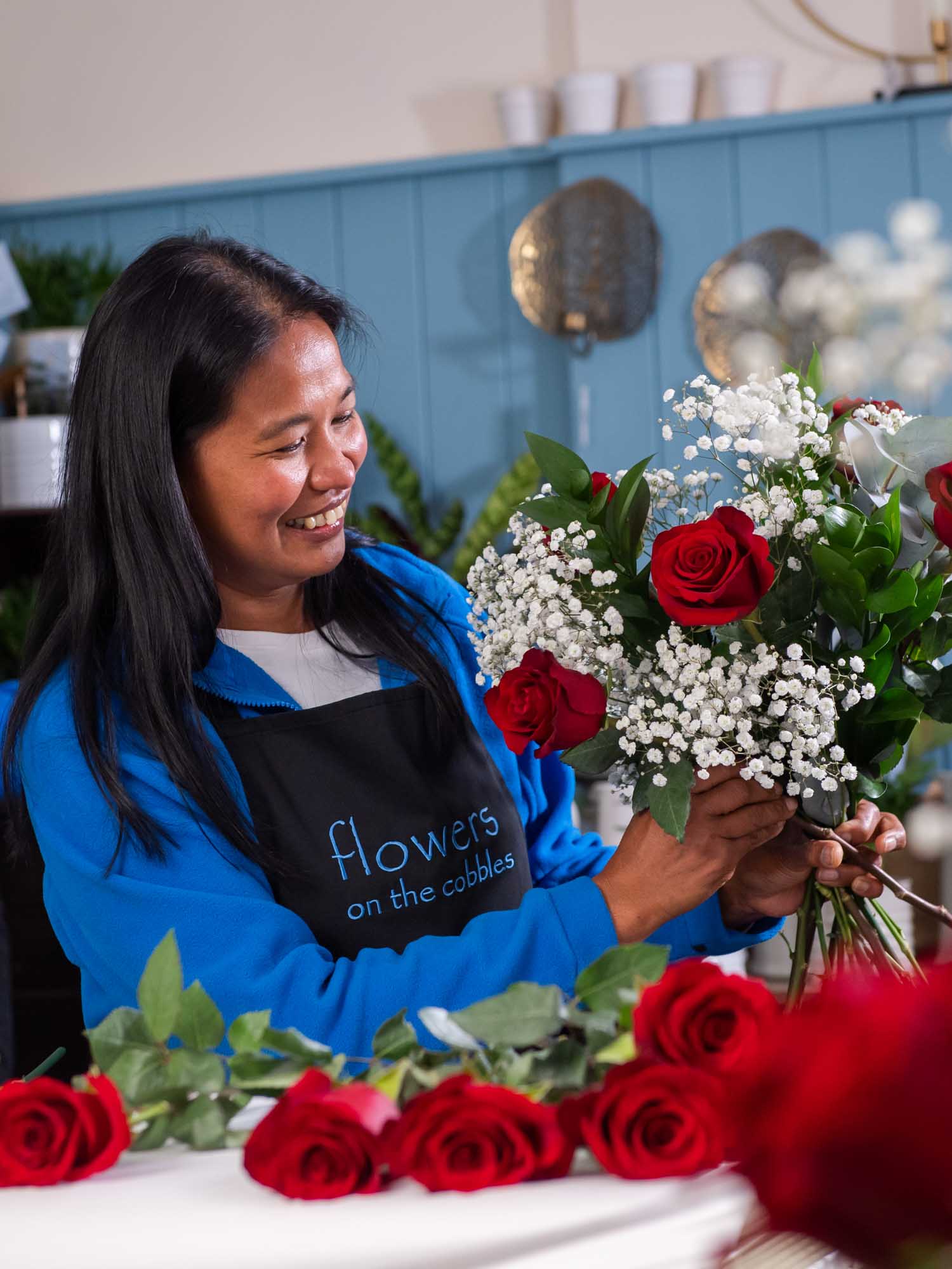 Florist arranging a bouquet of red roses and baby's breath with a smile.