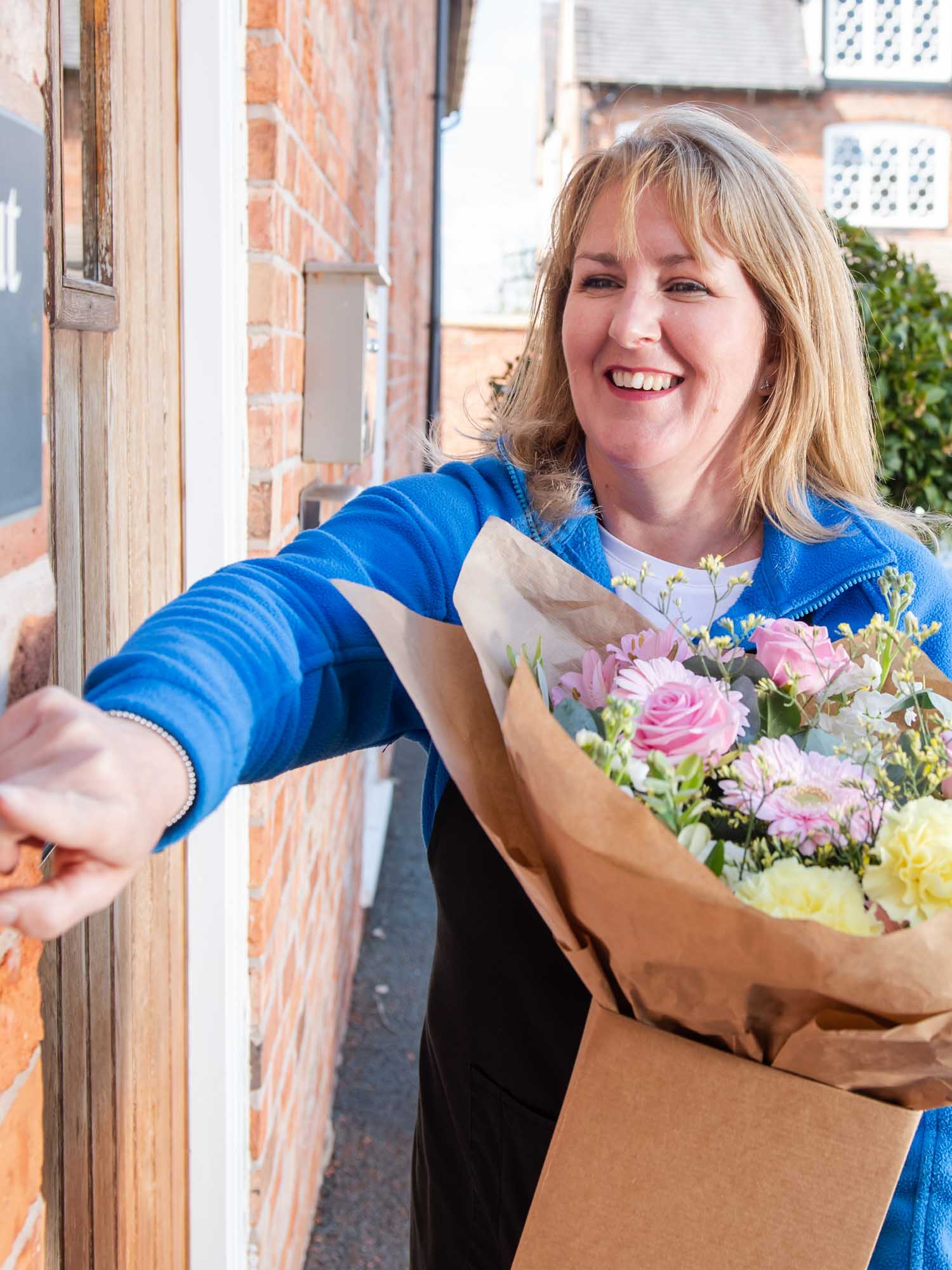 Florist rings doorbell as she hand delivers flowers.