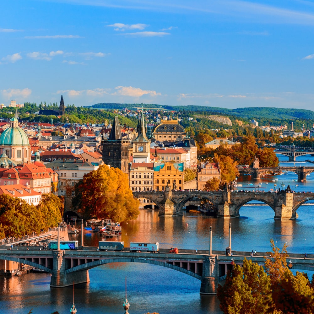 Prague skyline with Charles Bridge, the Vltava River, and historic spires at sunset.