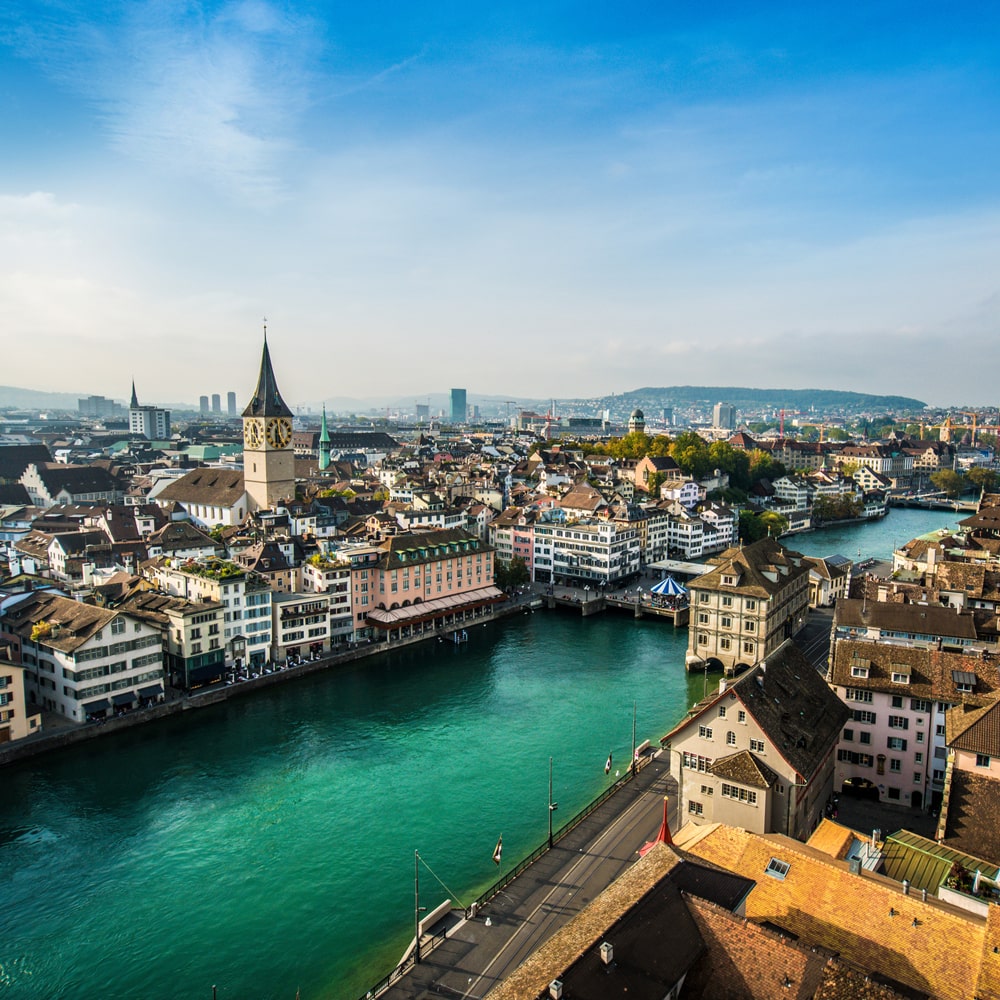 Zurich skyline with the Limmat River, historic buildings, and distant hills.