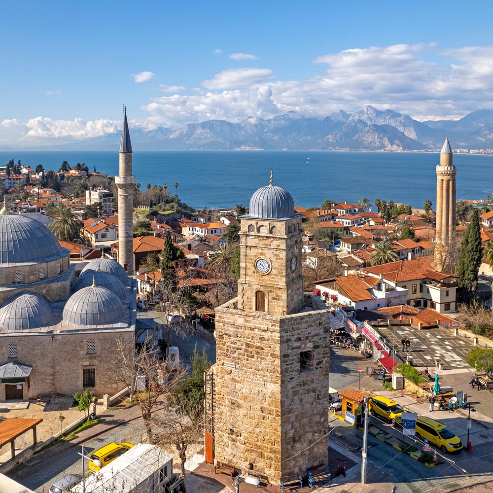 Antalya's old town with historic clock tower, mosques, and a coastal backdrop.