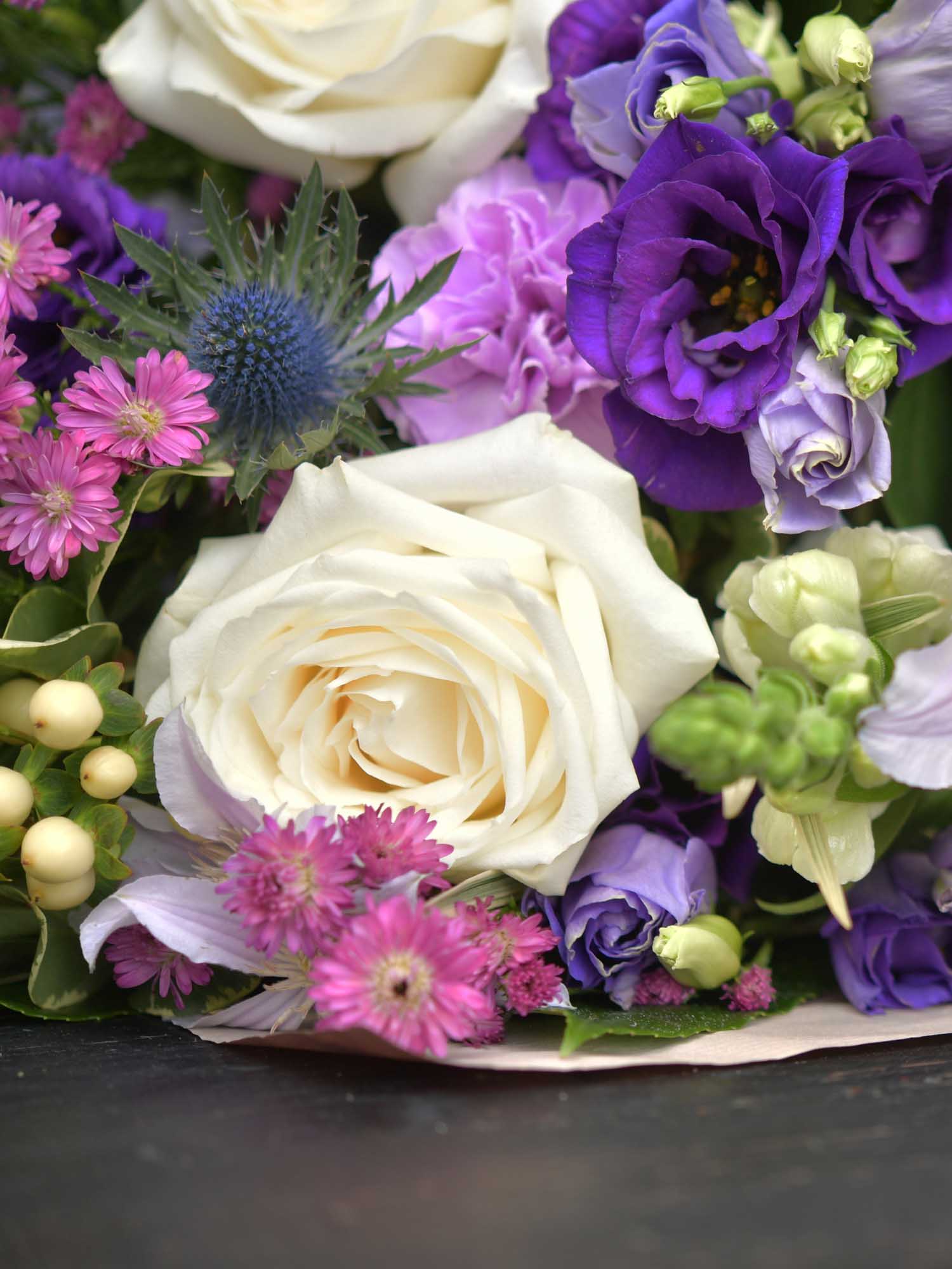 Purples and blues and whites are shown in this close up of funeral flowers being arranged by the local florist. Thistle is on display