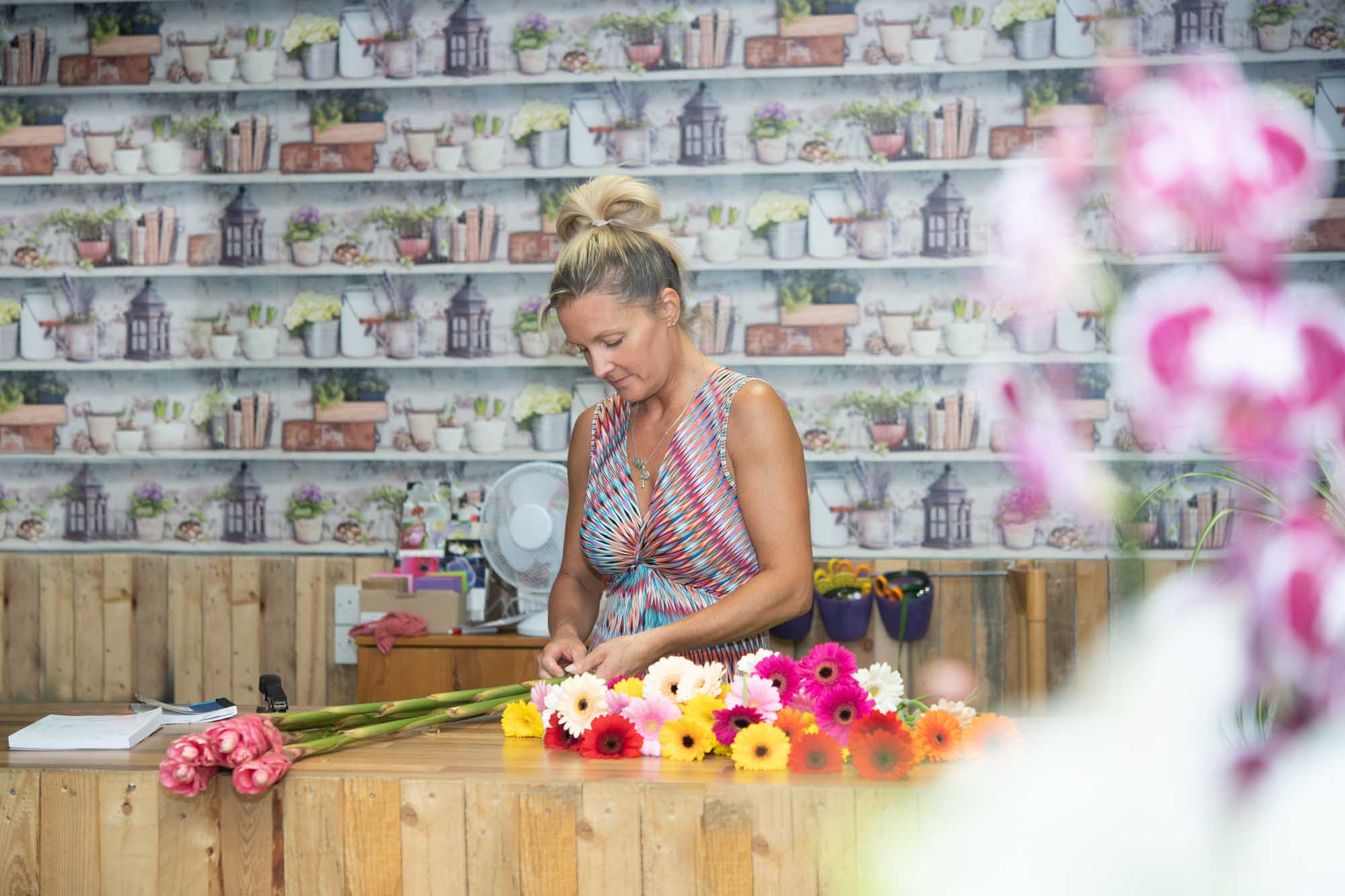 Florist arranging a bouquet of colorful gerbera daisies in a beautifully decorated flower shop.