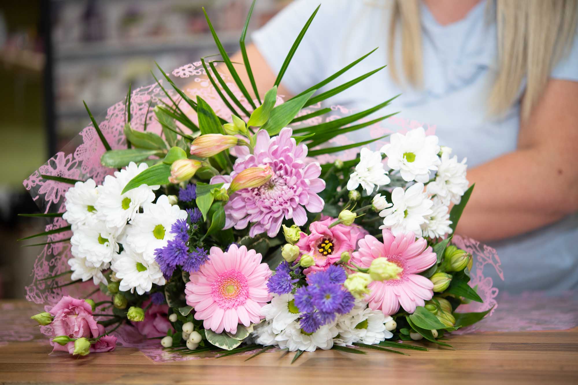 Pink wrap of flowers in pink, white and blue layed on a table being made by a florist.