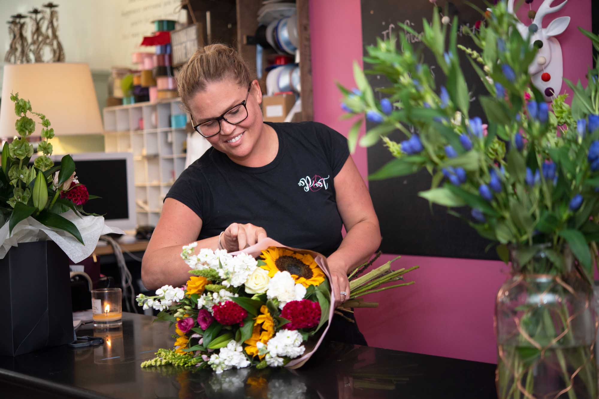 Florist making an eco-wrap featuring sunflowers and snapdragons layed on a worktop in the flowershop