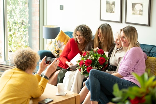 Family sitting together on settee with birthday card and bouquet of flowers. Everyone smiling.