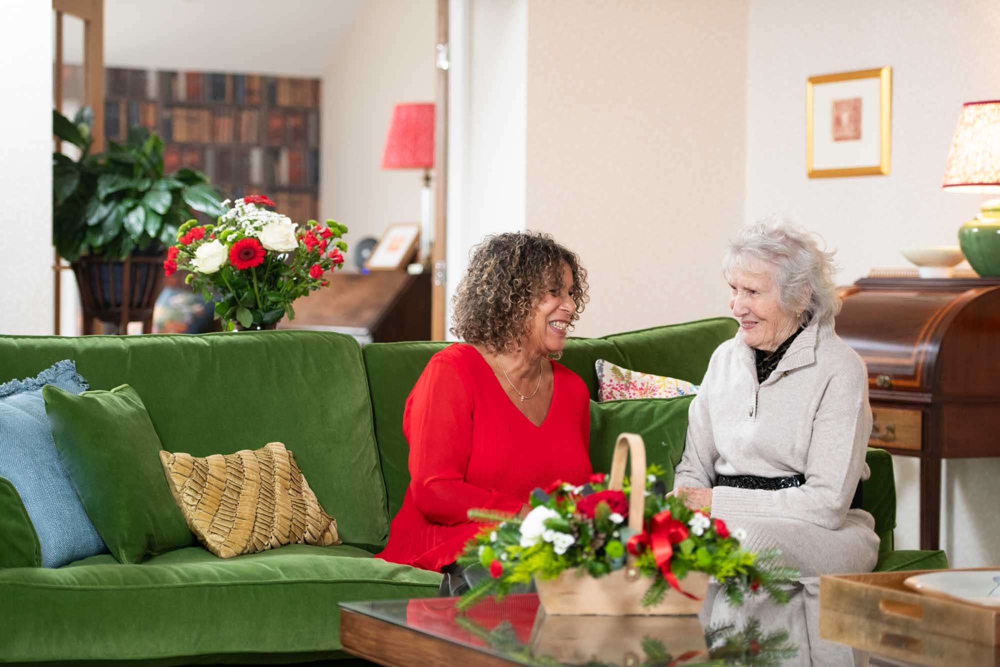 2 ladies chatting in comfortable surroundings of a new home. Flowers are on the coffee table