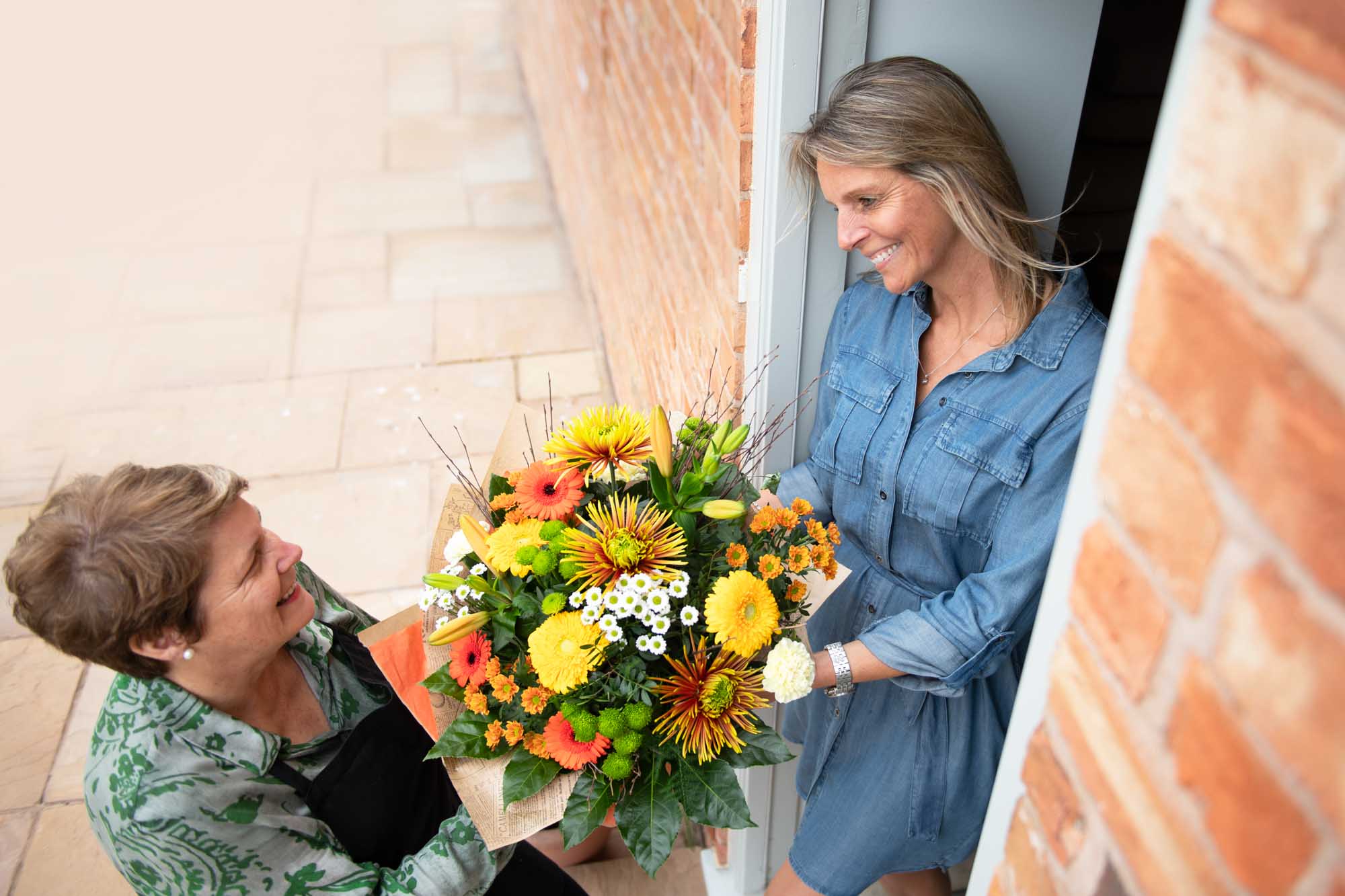 Overhead shot of a florist in an apron delivering autumn themed flowers to a woman wearing a denim dress.