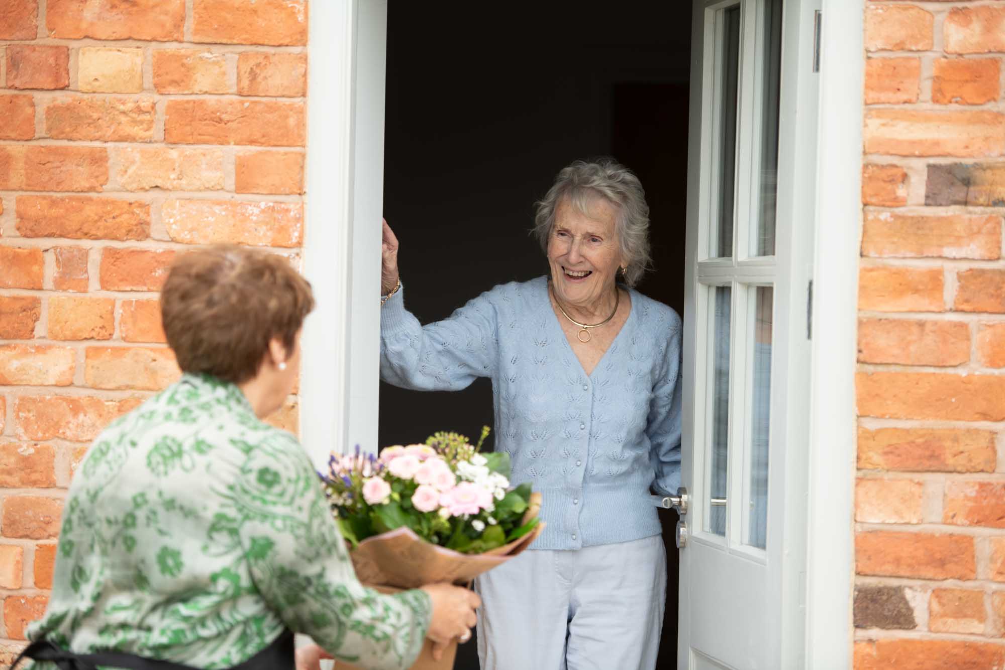 Florist hand delivers bouquet to smiling elderly lady at the door.