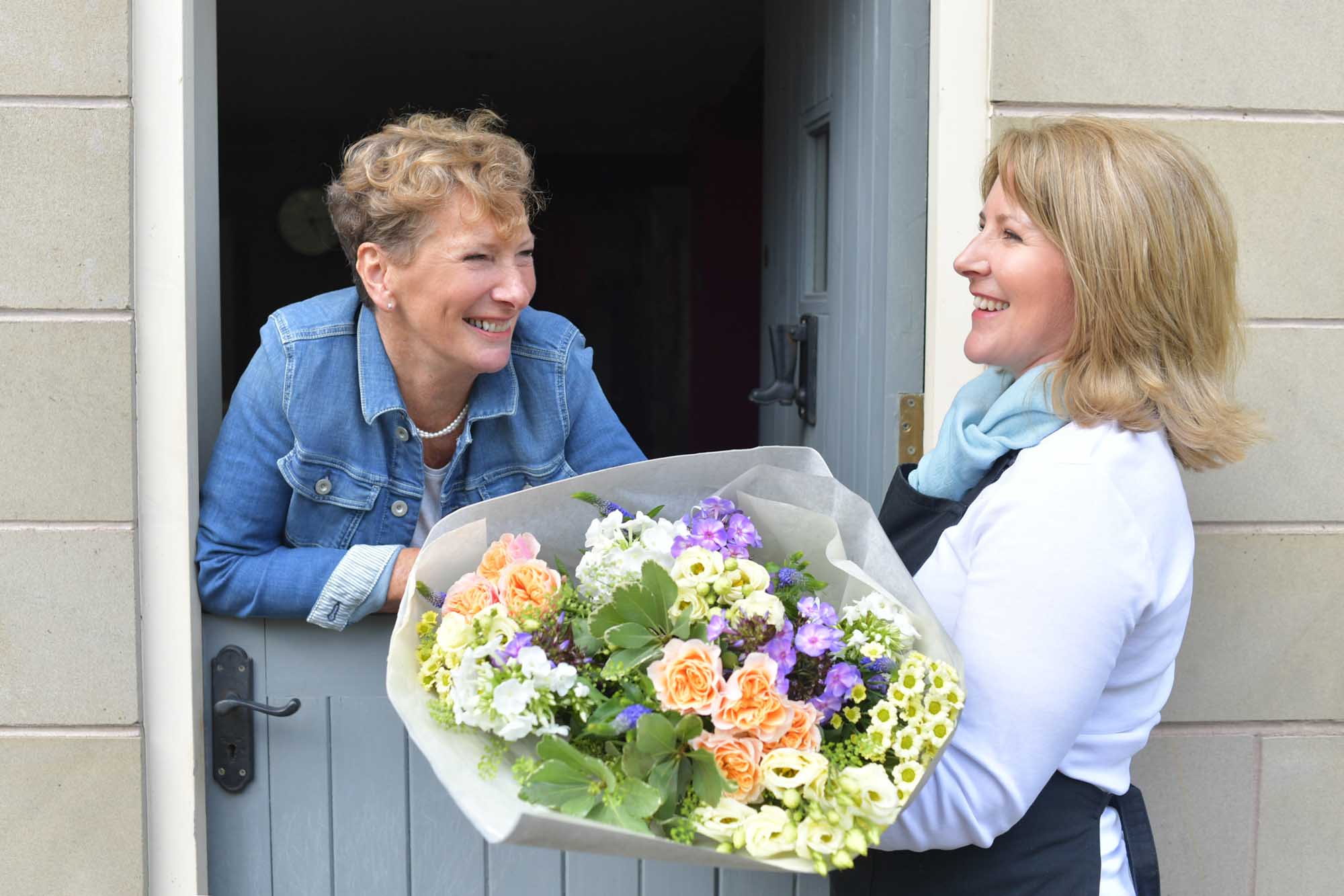 Florist delivering a purple and peach themed wrap of flowers in conversation with the happy recipient