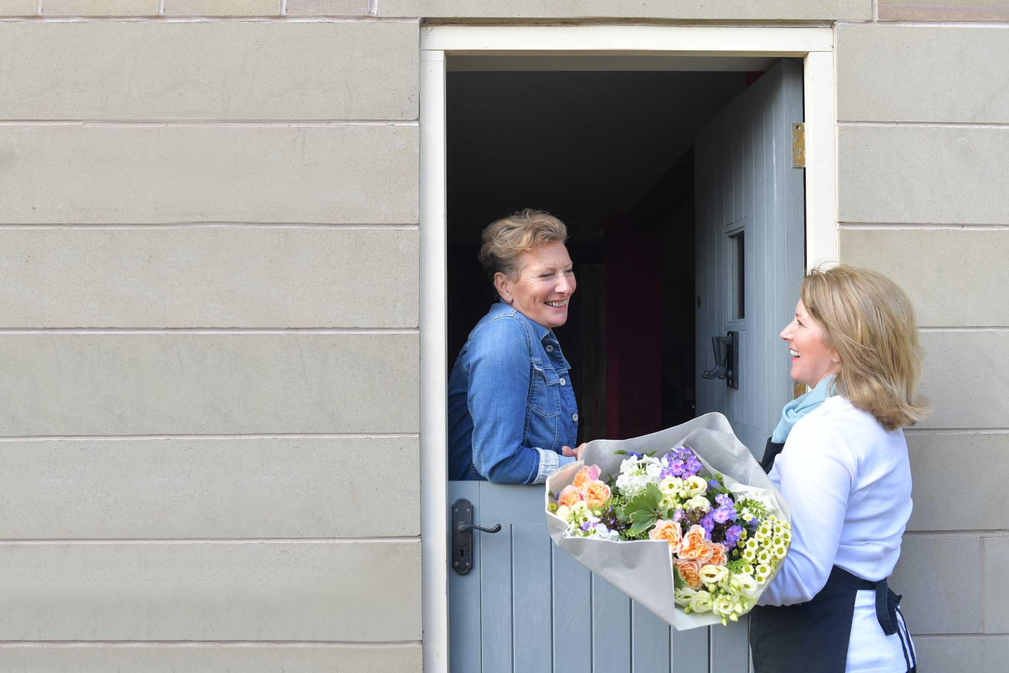 Smiling customer receiving summer flowers at her door delivered by local florist