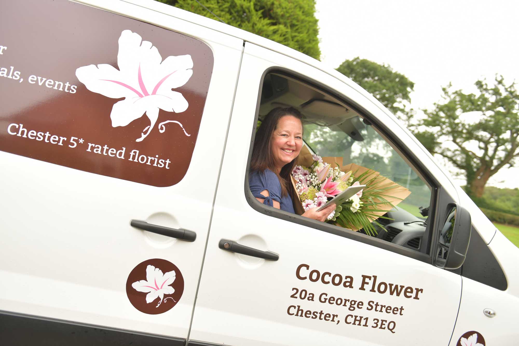 Florist in delivery van holding a bouquet and smiling whilst looking for the delivery address.