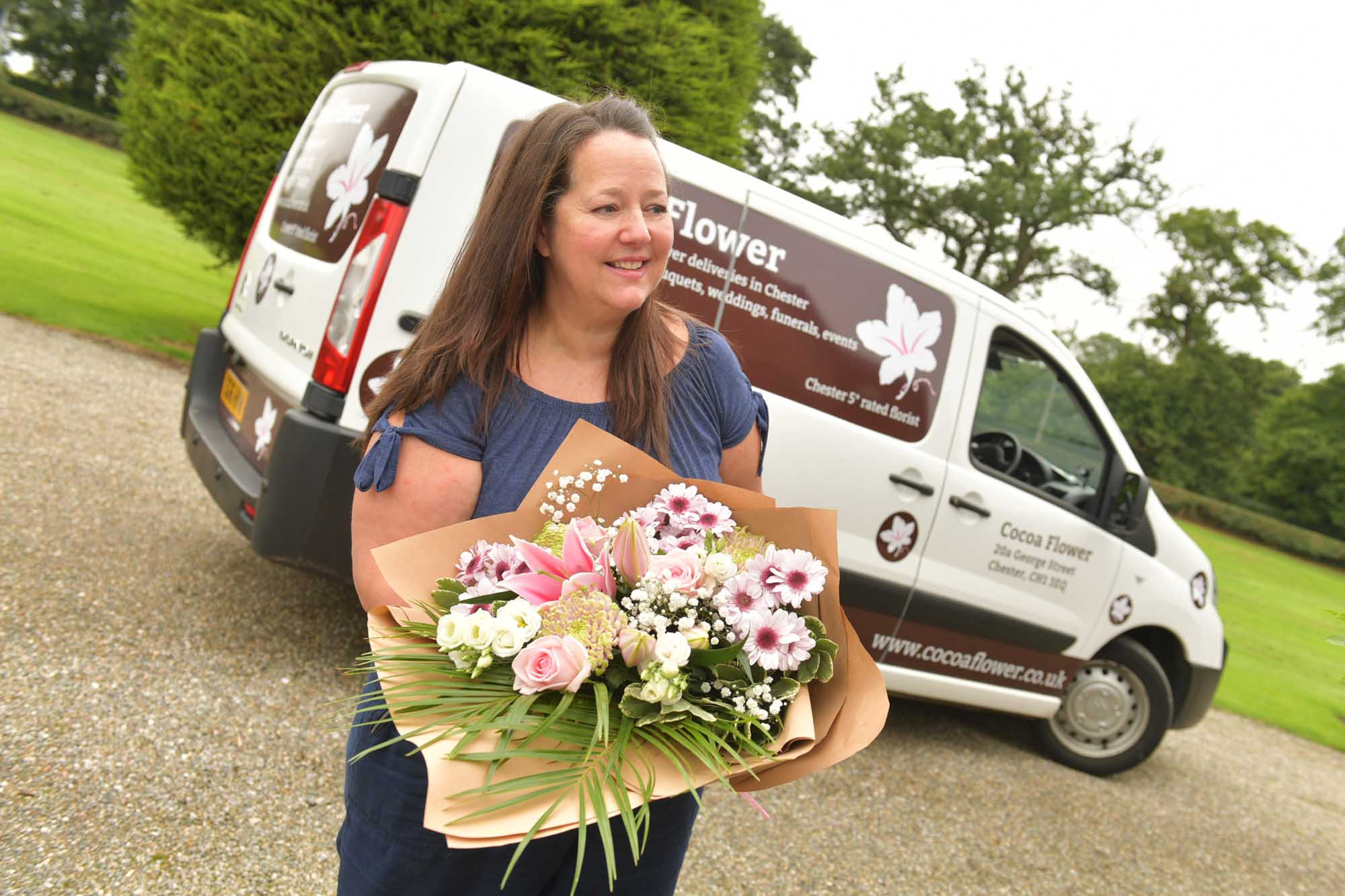 Florist outside holding a wrap of pastel themed flowers with a branded delivery van in background.