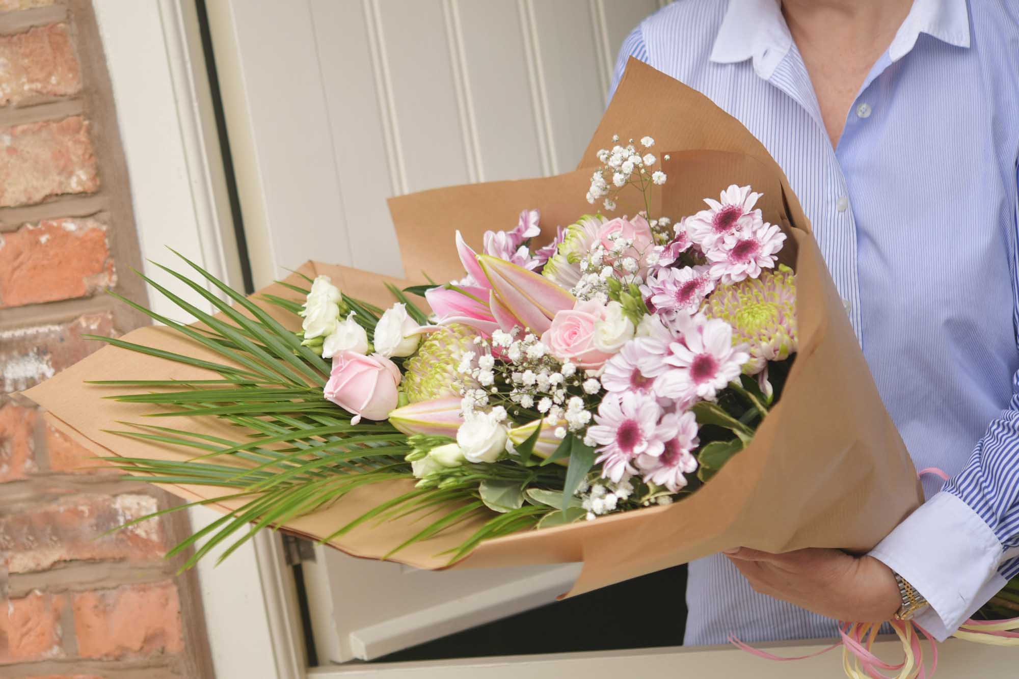 Crop of a woman in a light blue shirt holding a eco-wrap of pastel themed flowers