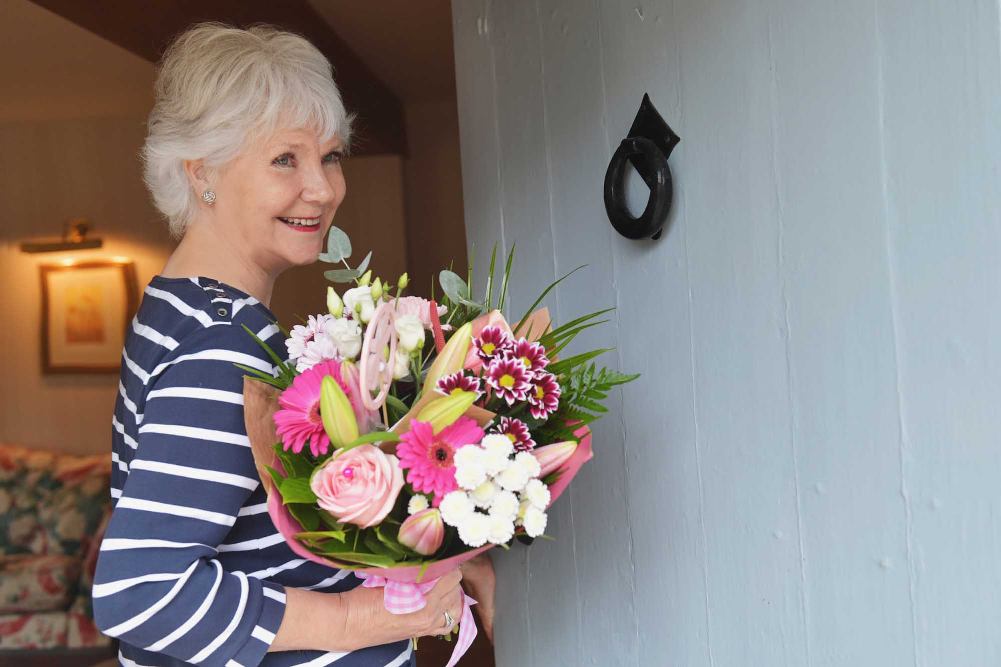 Older woman smiling with flowers delivered in hand about to close the door