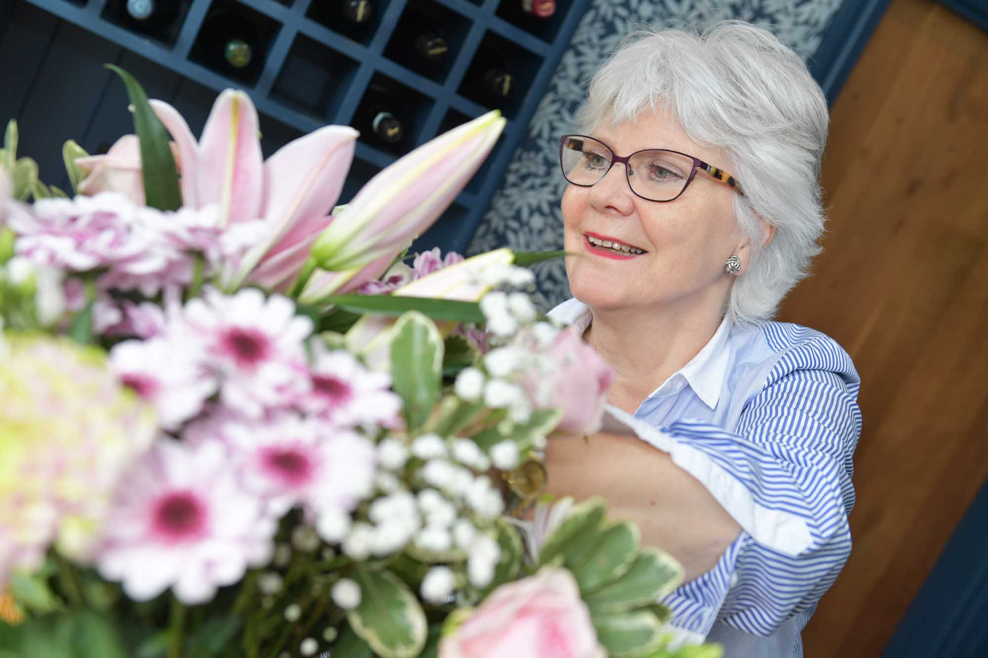 Happy older woman in her home reworking a flower arrangement