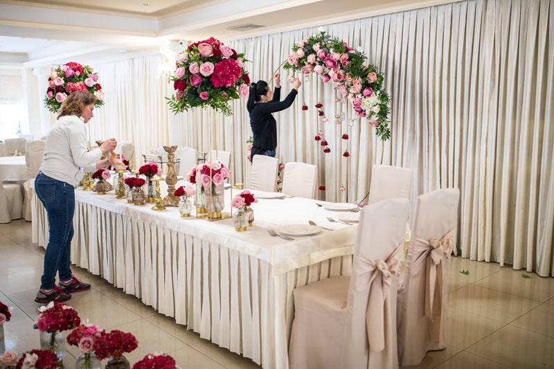 Florists arranging pink and red floral decorations at an elegant wedding venue.