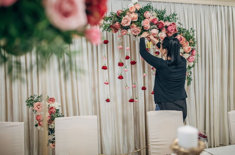 Florist arranging pink and red floral decorations at a wedding venue.