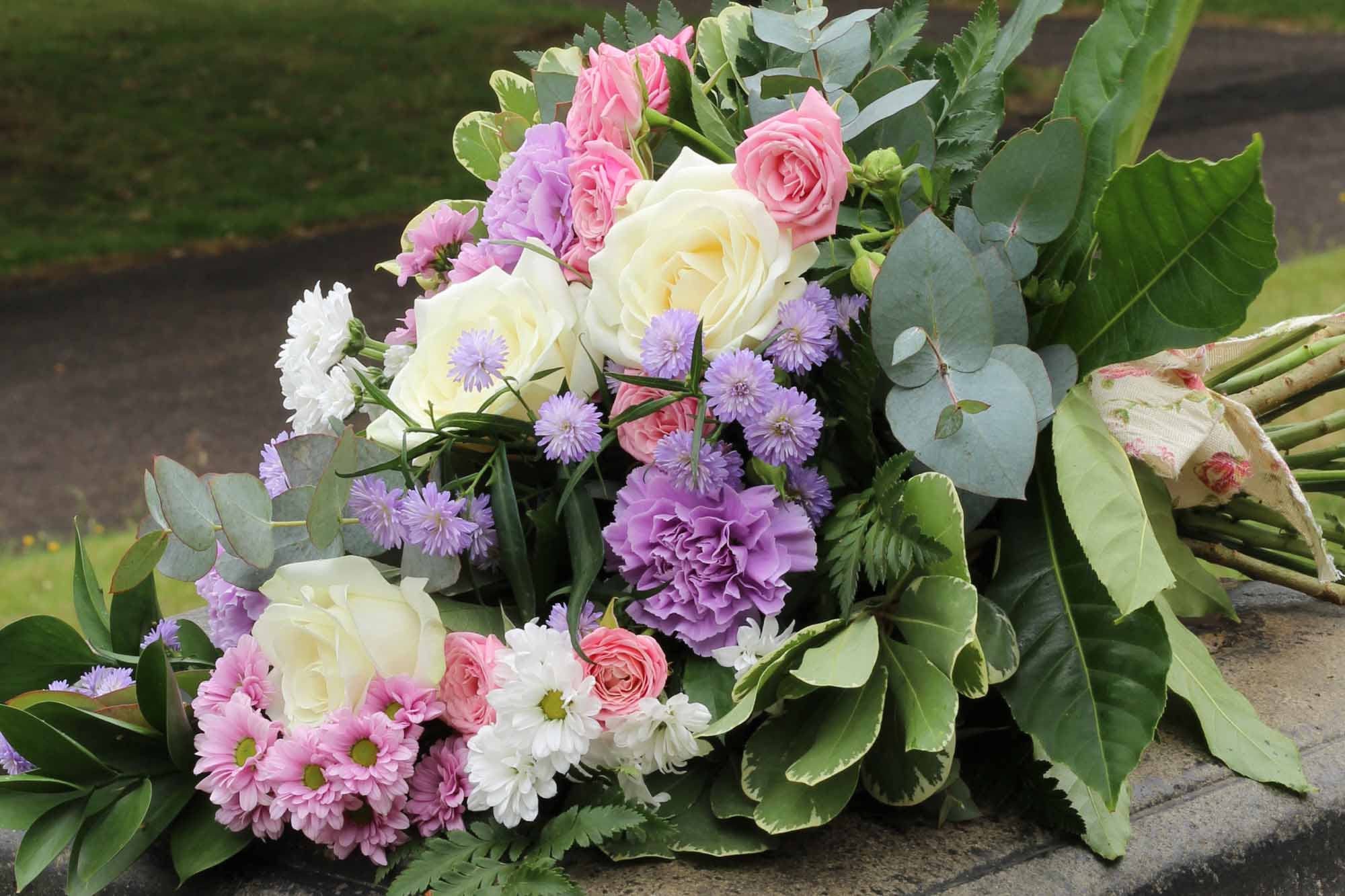 Funeral tied sheaf with white roses, pink and lilac flowers on stone ground.