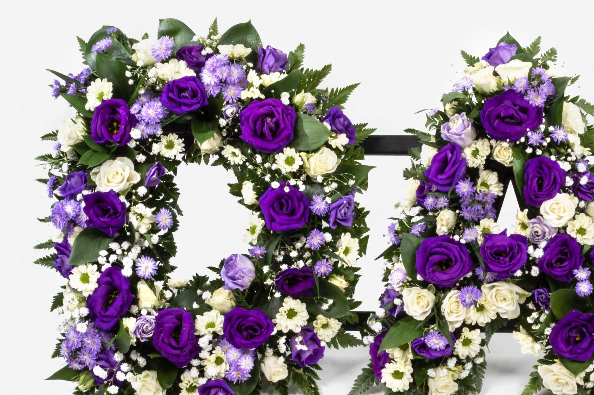 Close-up of D and A from a DAD funeral letter arrangement in purple and cream flowers on a white background.