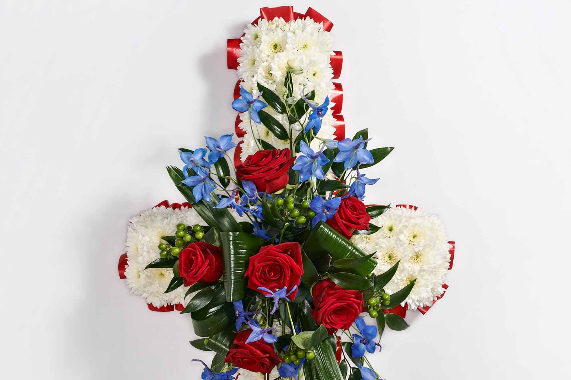 Close-up of a large funeral cross with white chrysanthemums, red roses, and hints of blue flowers.