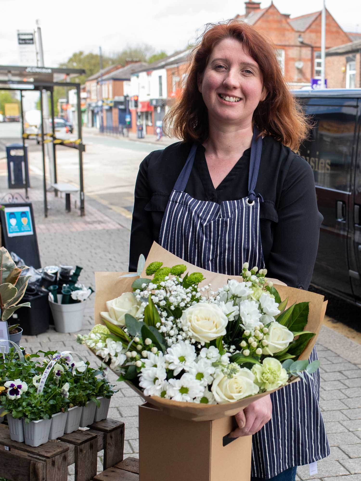 Florist smiling while holding a bouquet of white flowers on a city street.