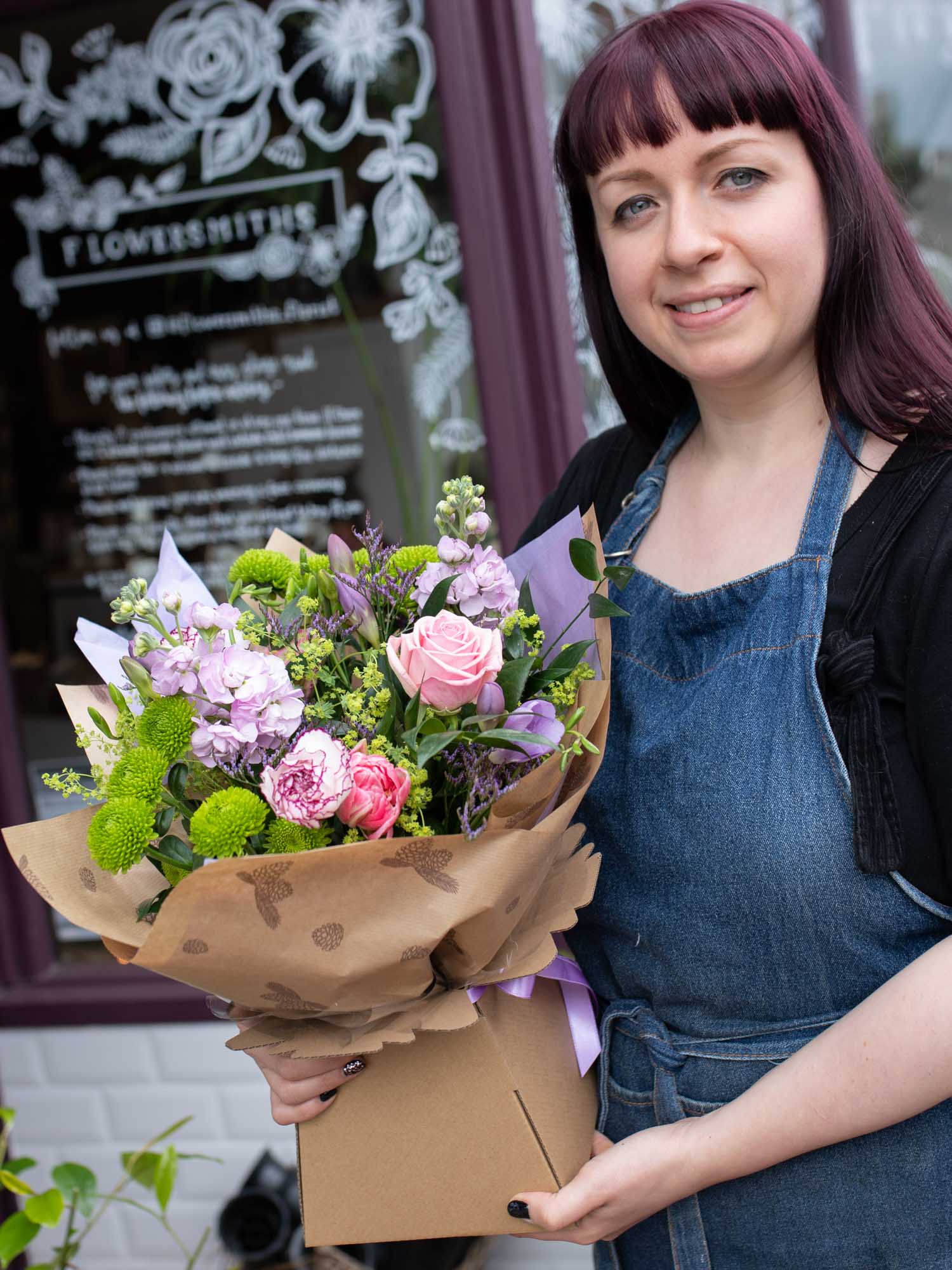 Florist in front of shop ready to deliver a pink and purple hand-tied