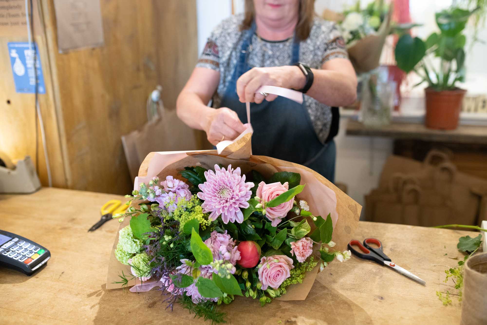 Florist tying ribbon around a handtied layed on worktop in a flowershop