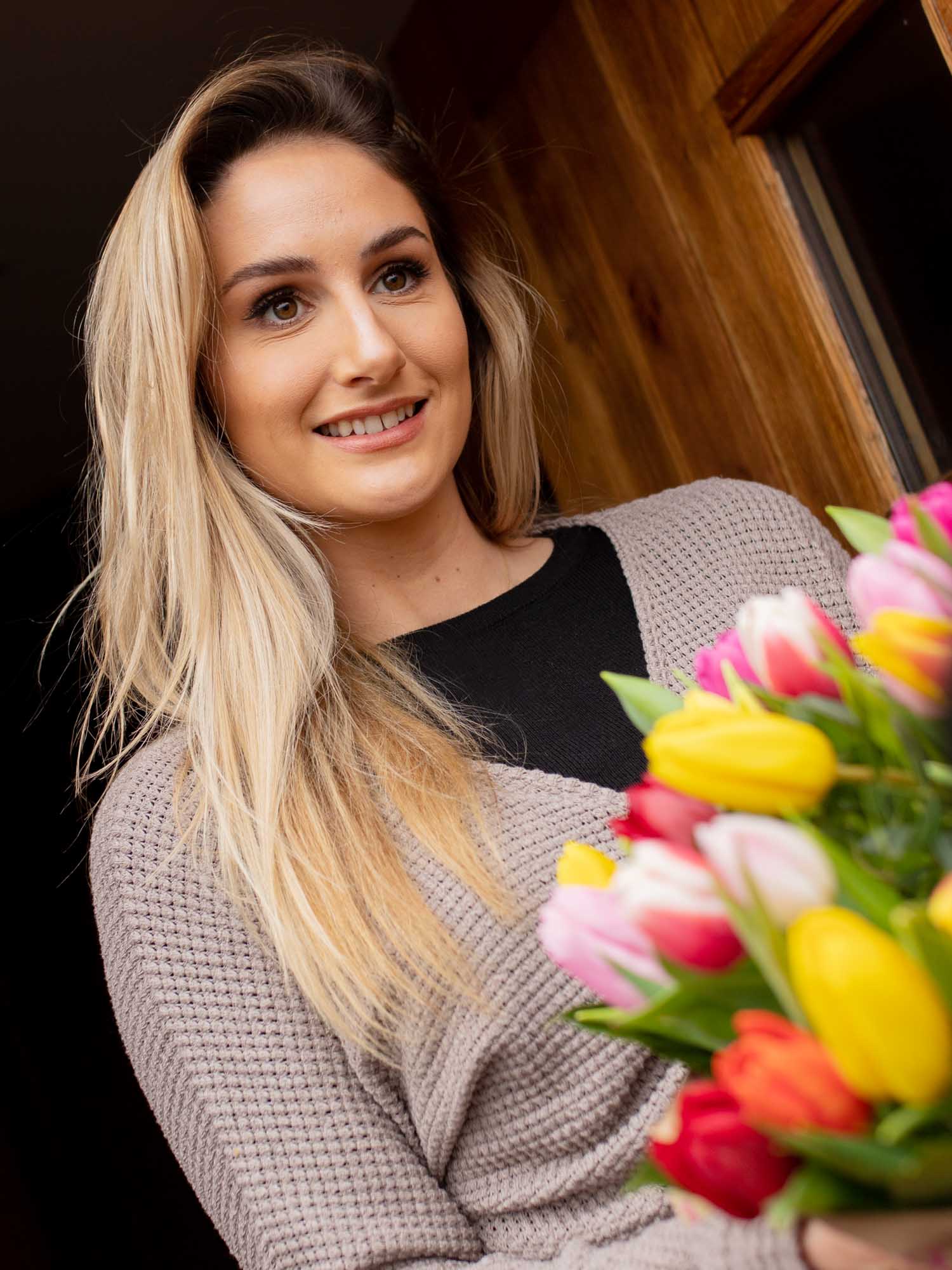 Beautiful young lady holding bouquet of tulips at the door.