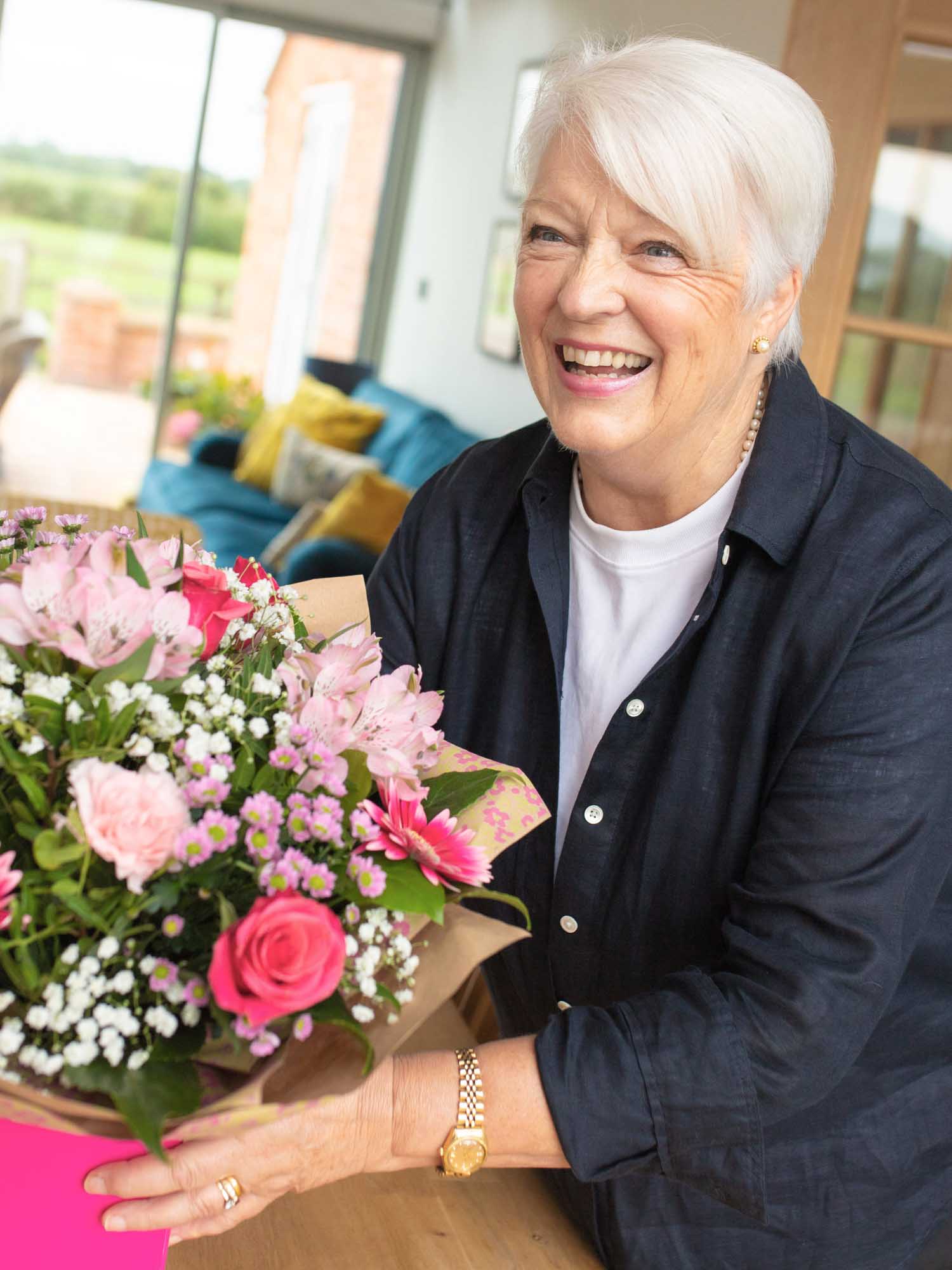 Smiling woman holding a bouquet of pink flowers in a bright, modern home