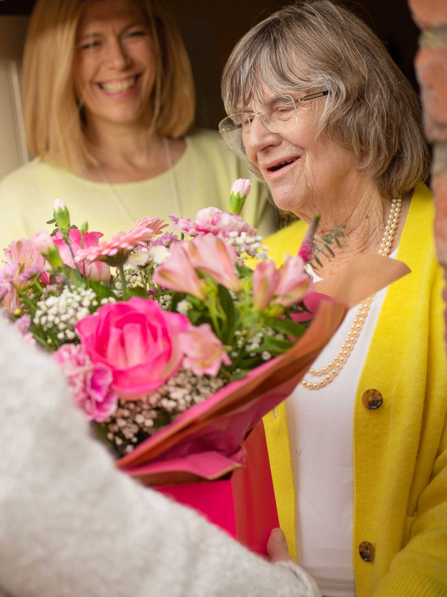 Florist delivering beautiful pink flowers to an elderly lady at the door.