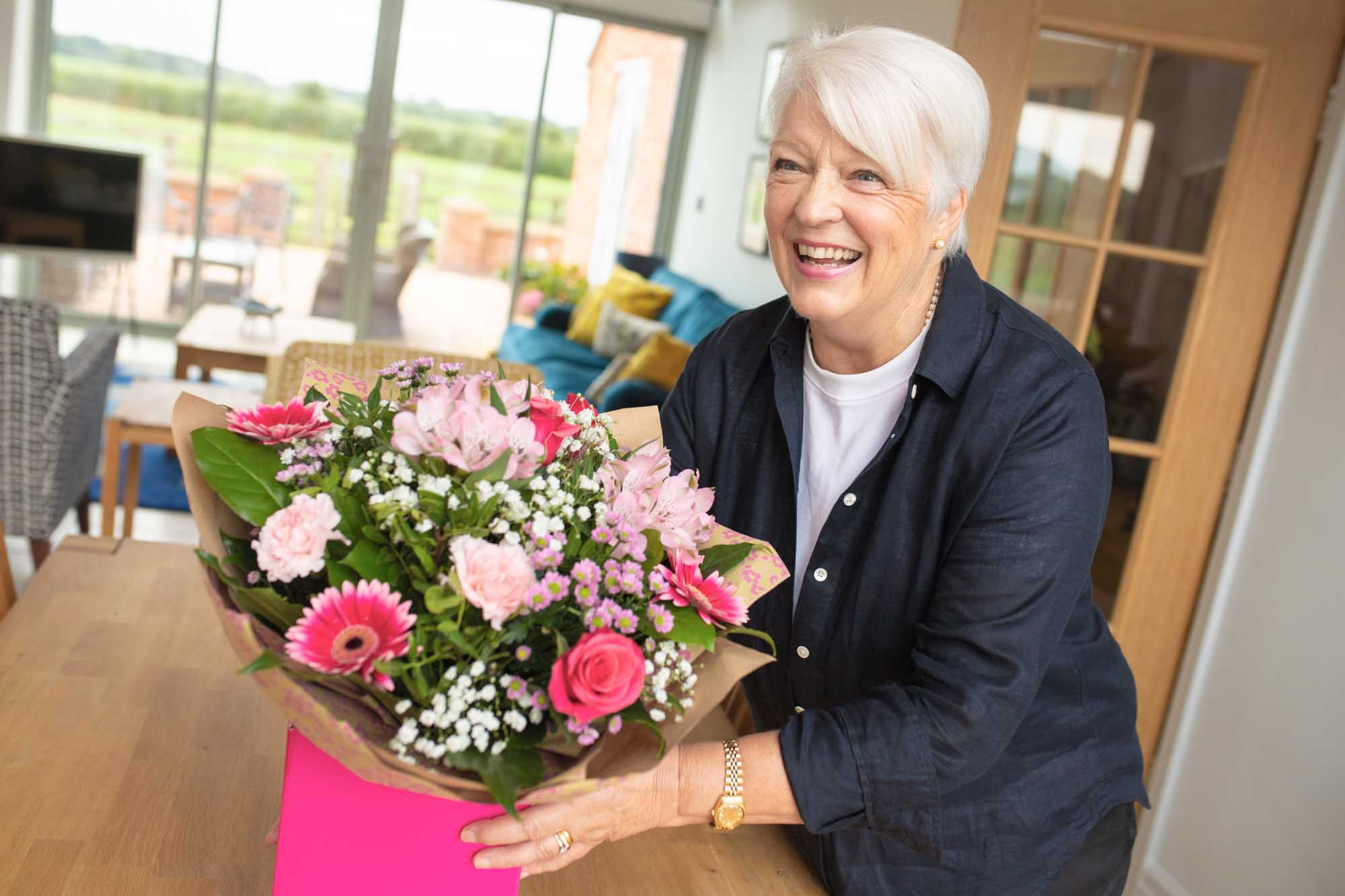 Smiling older woman in living room placing a hand-tied bouquet on a table