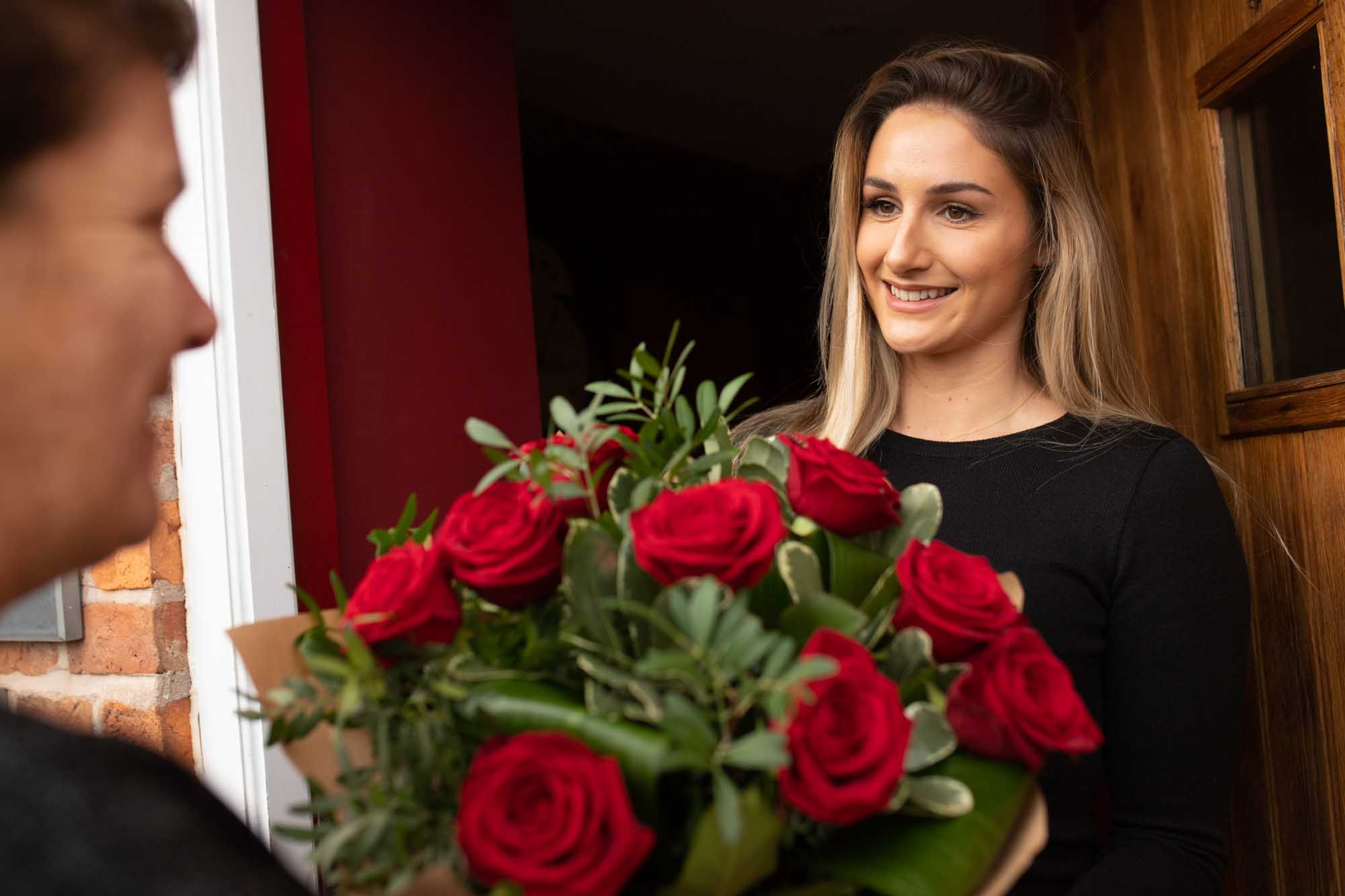 beautiful recipient of red roses stands at the door holding the red roses just delivered same day by the local irish florist