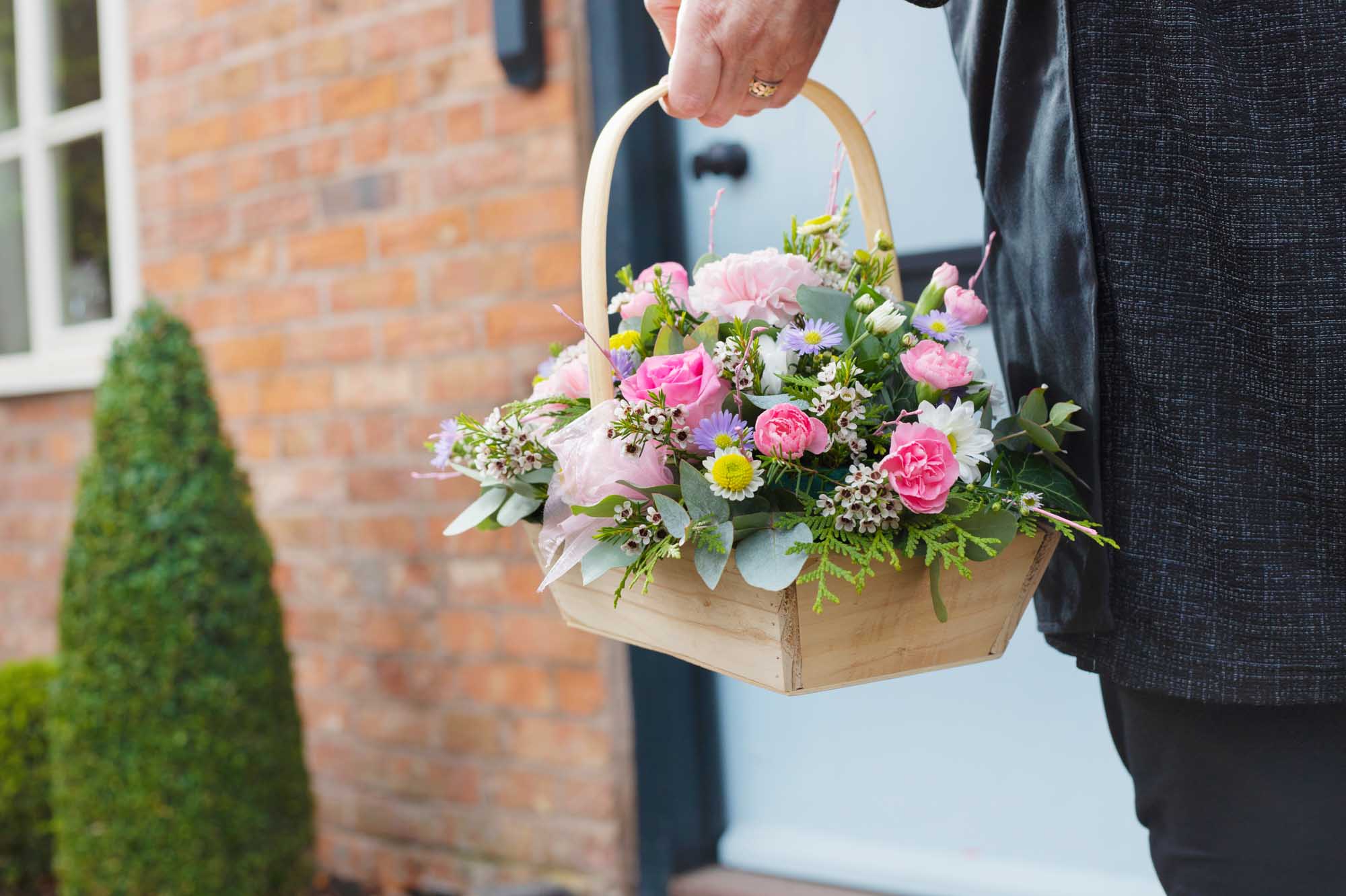 Woman holding a pastel themed flower basket with a front door in the background about to make a delivery