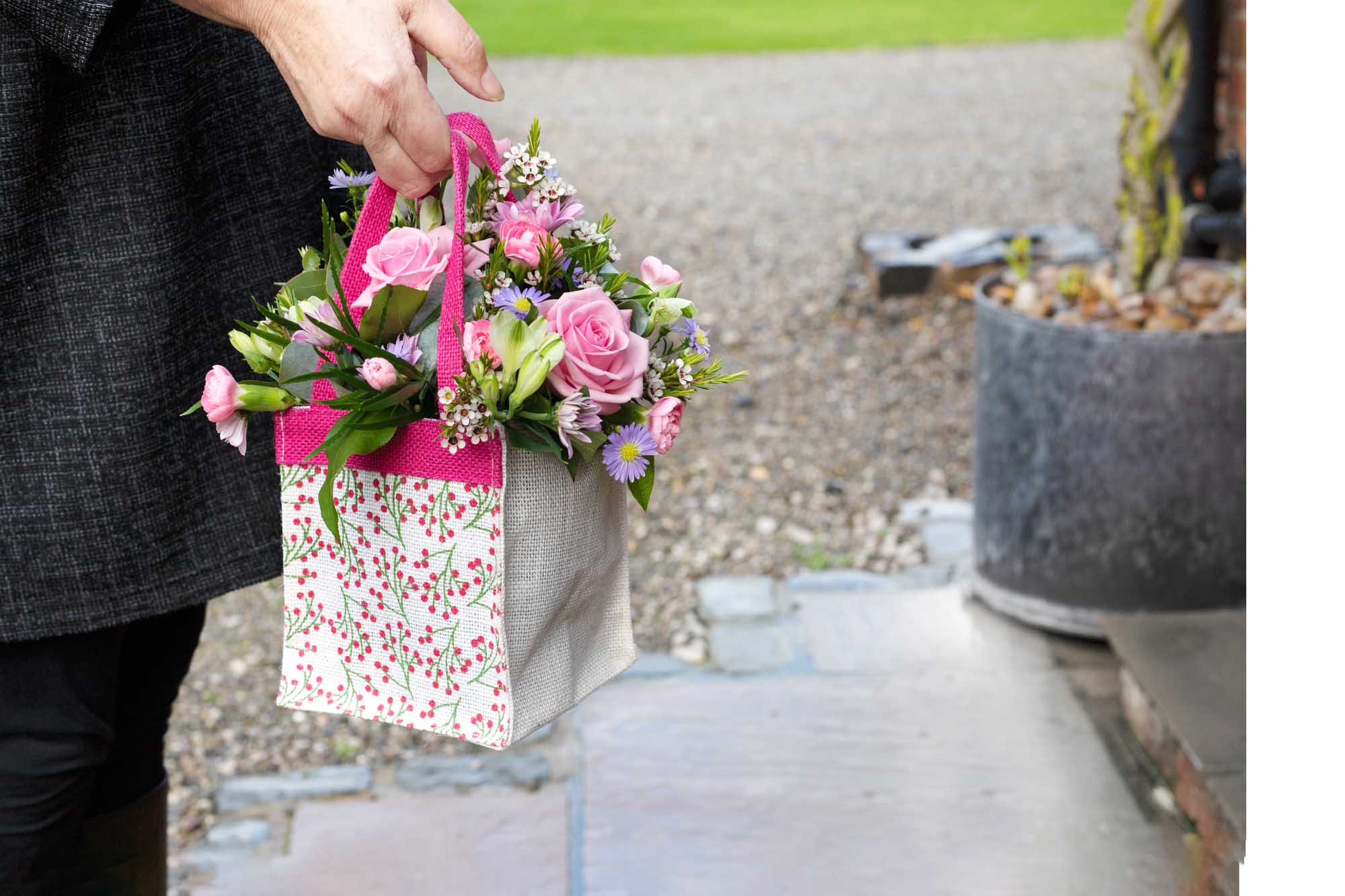 Hand holding a hessian bag on of pastel themed flowers about to be delivered.