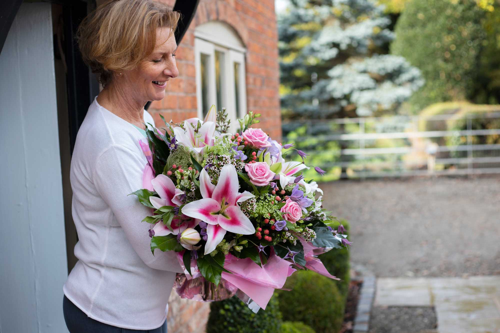 Side on view of a happy woman at her front door looking down at the luxury bouquet that was delivered