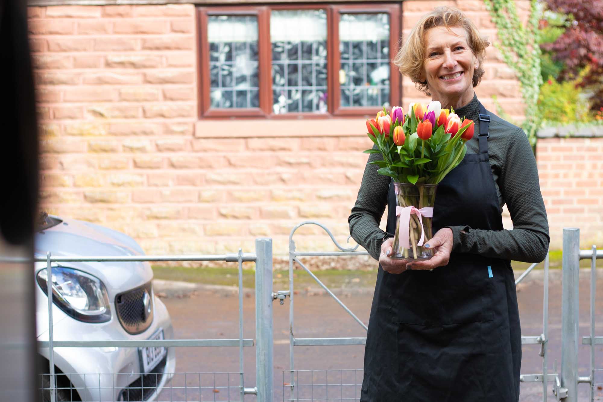 Smiling florist outside a house holding a vase of tulips about to be delivered.