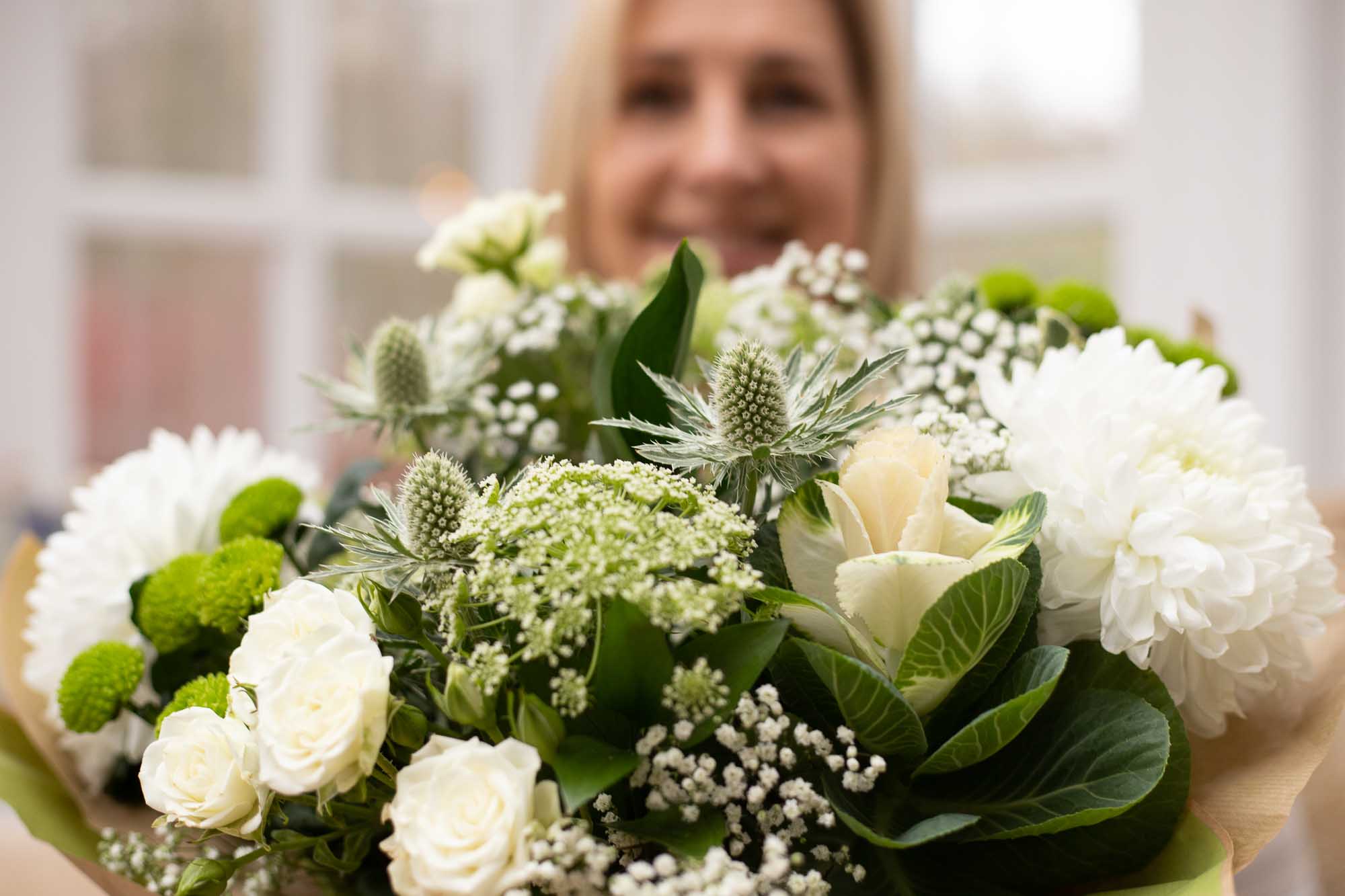 Bokeh of a womans face in a background and a large close-up of white themed flowers in foreground.