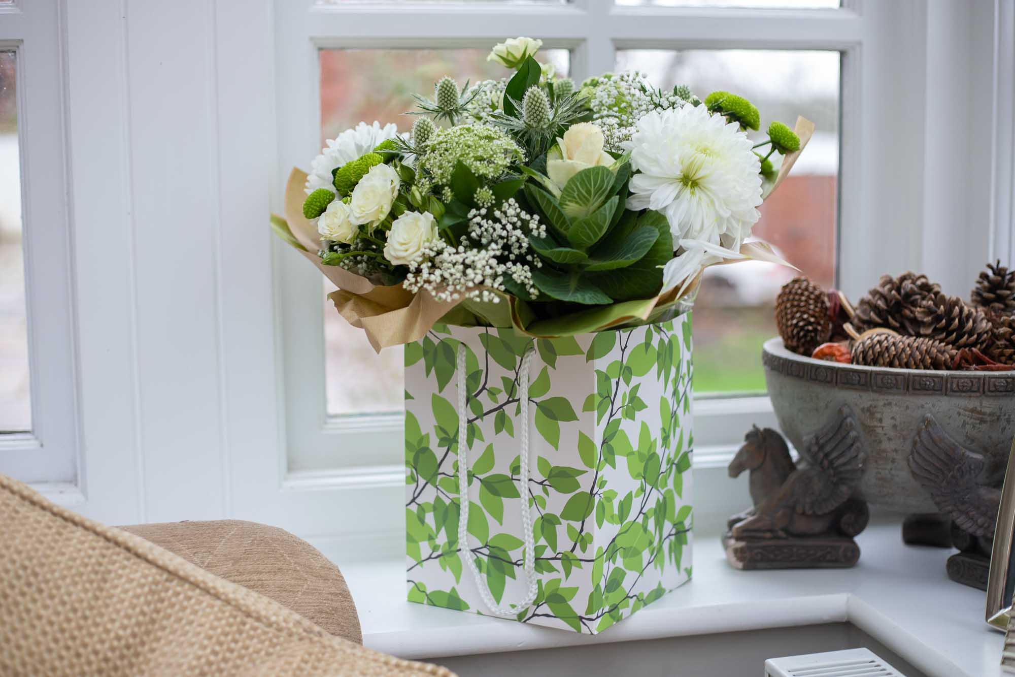 Cream and green themed box of flowers placed on a window ledge in a modern interior setting.